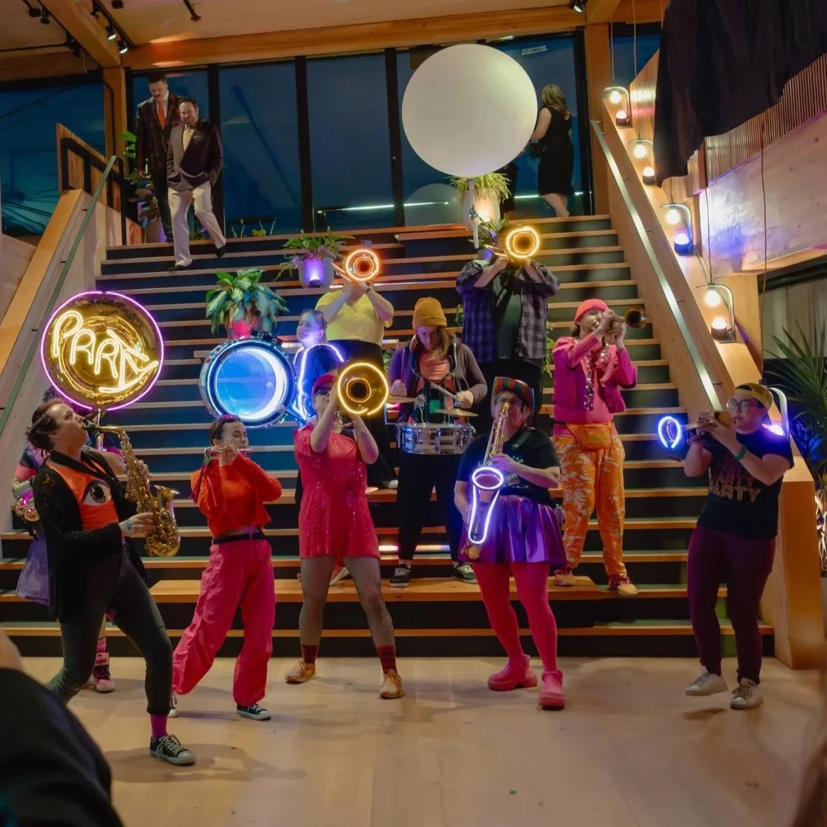A marching band wrapped in neon lights descends a staircase.