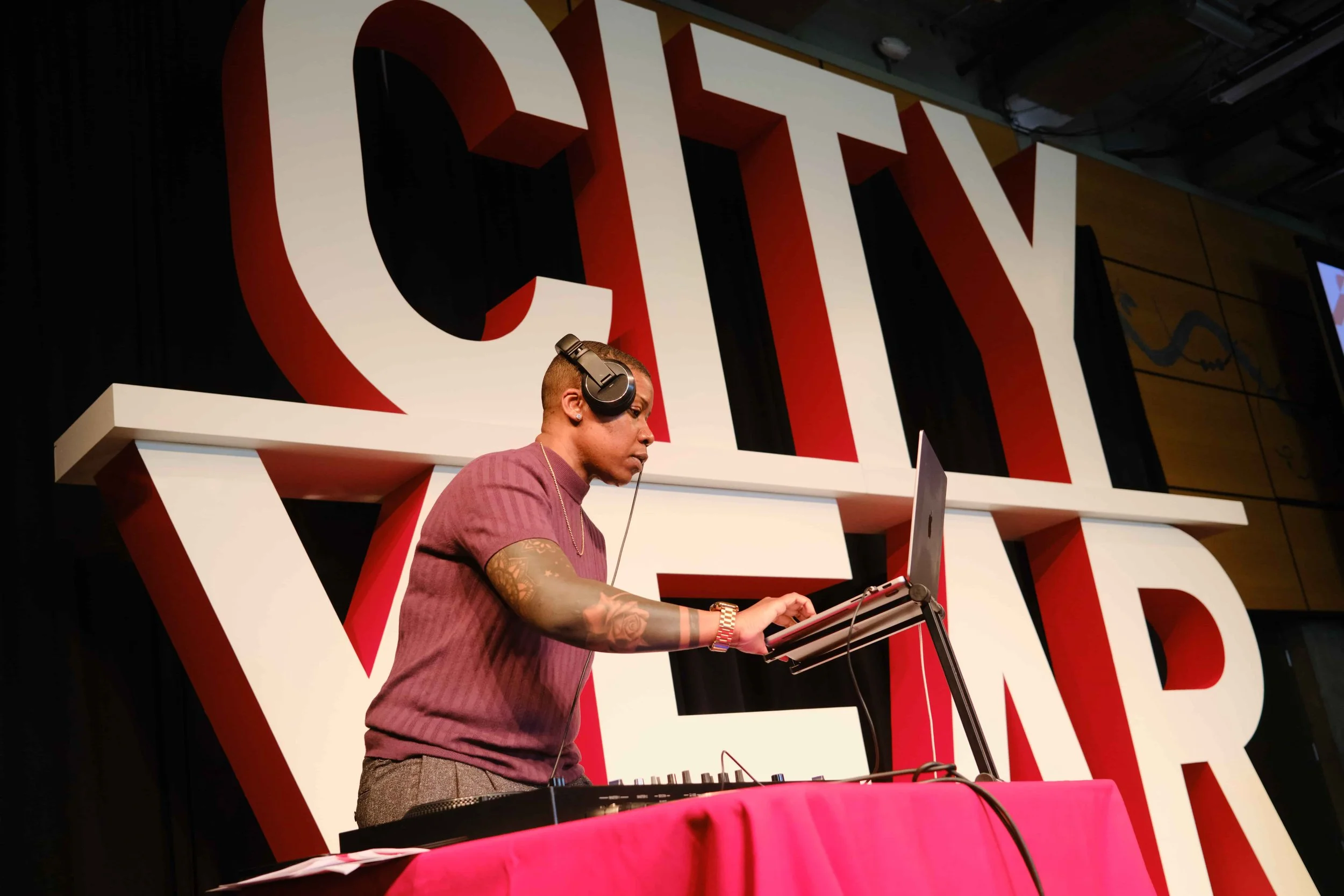 A DJ is performing on stage with giant block letters behind them reading "CITY YEAR"