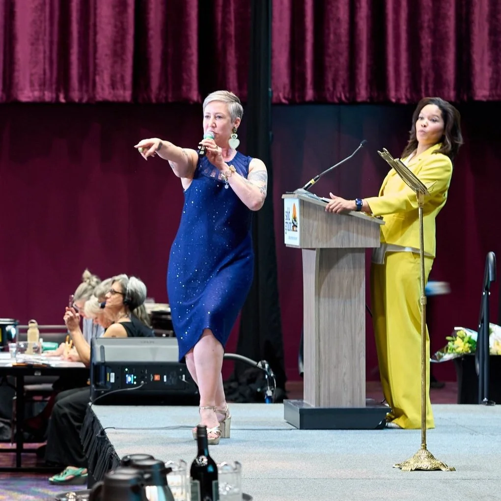 A woman wearing blue and a woman wearing yellow onstage together
