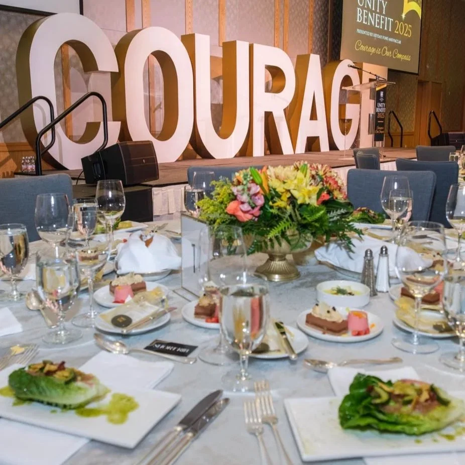 A dining table is set for an elegant meal, and large letters spelling "Courage" are seen in the background.