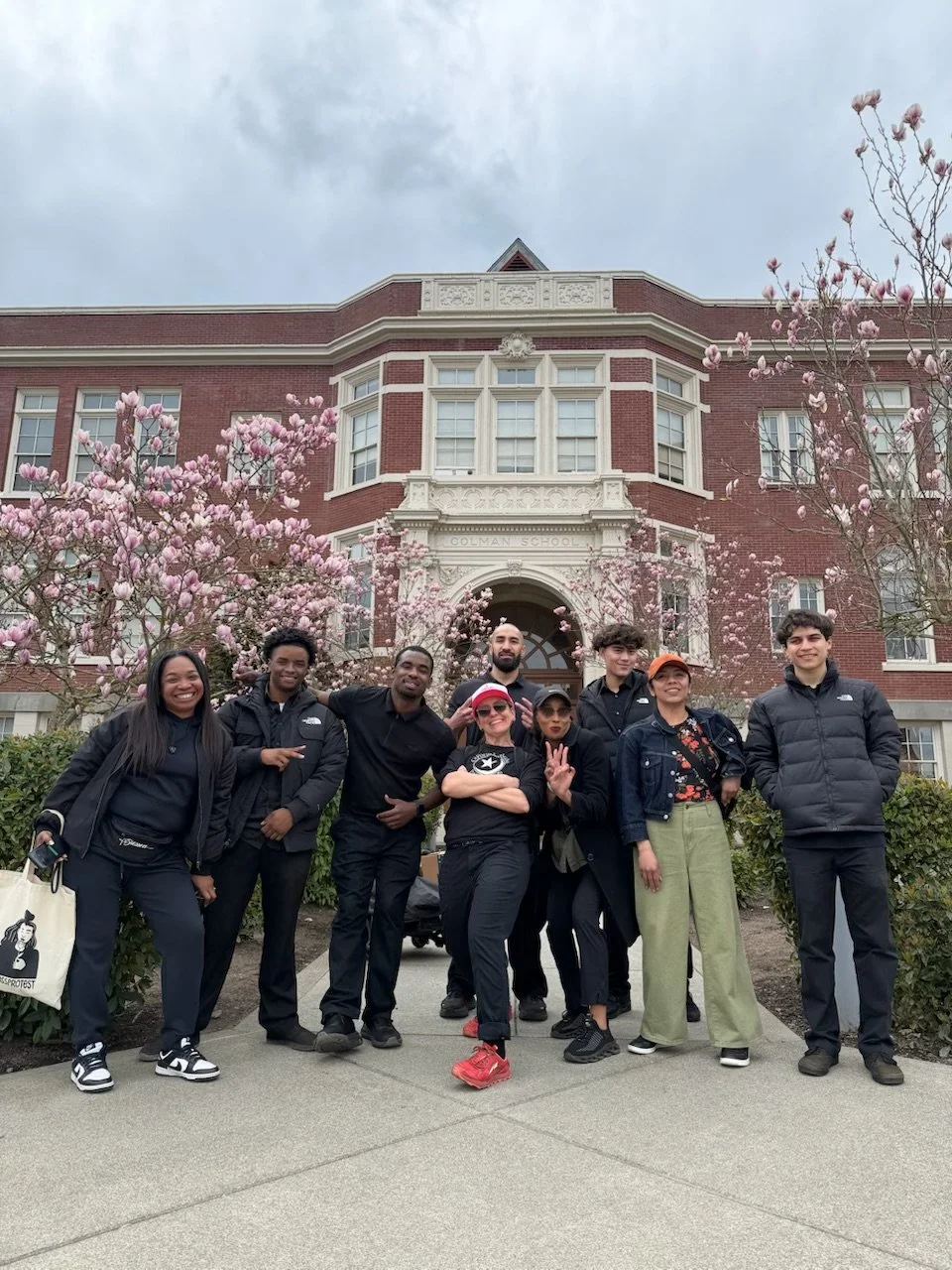 A group of people are standing happily in front of a brick building.