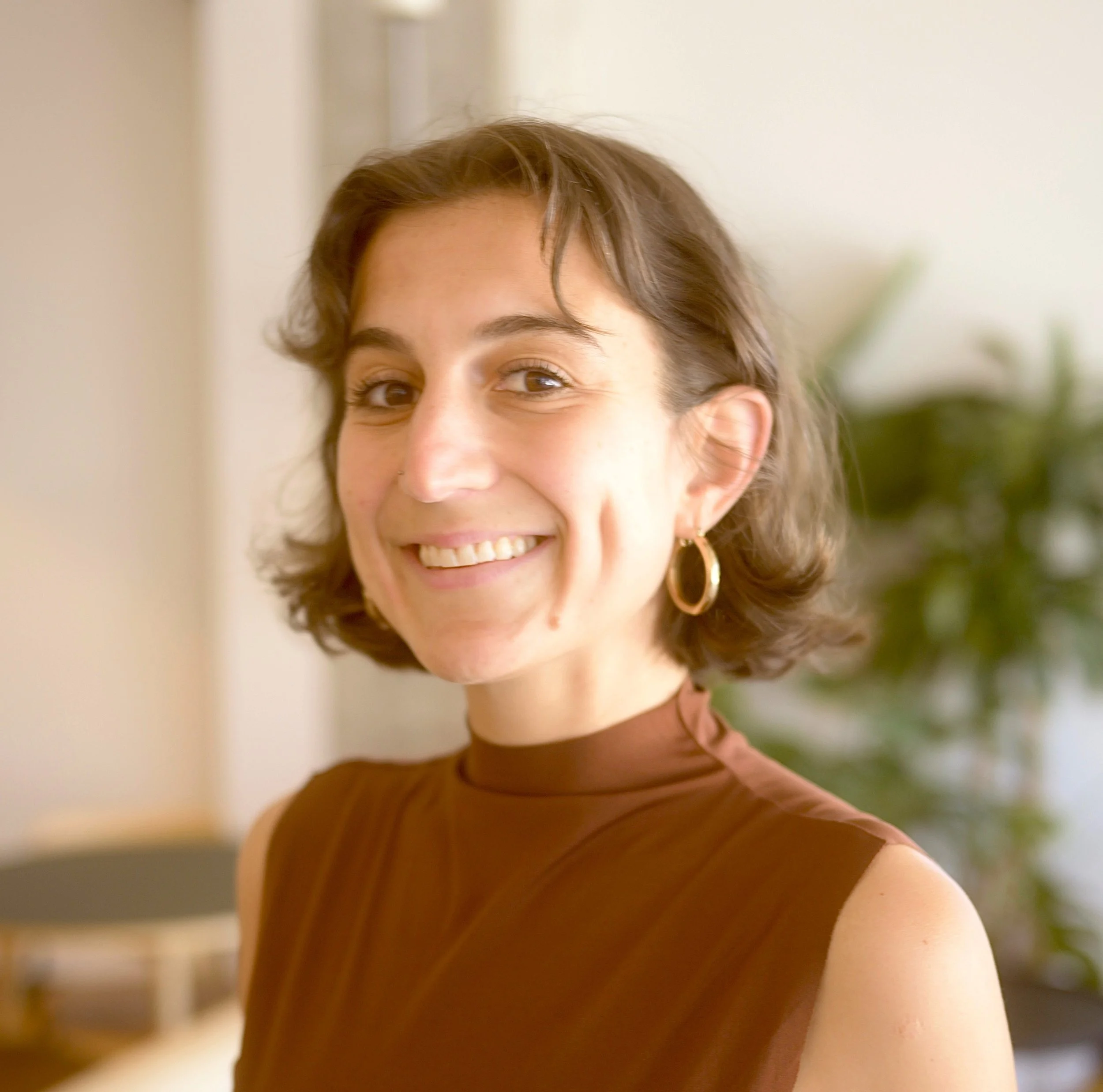 A white woman with brown hair and wearing a brown top smiles brightly.