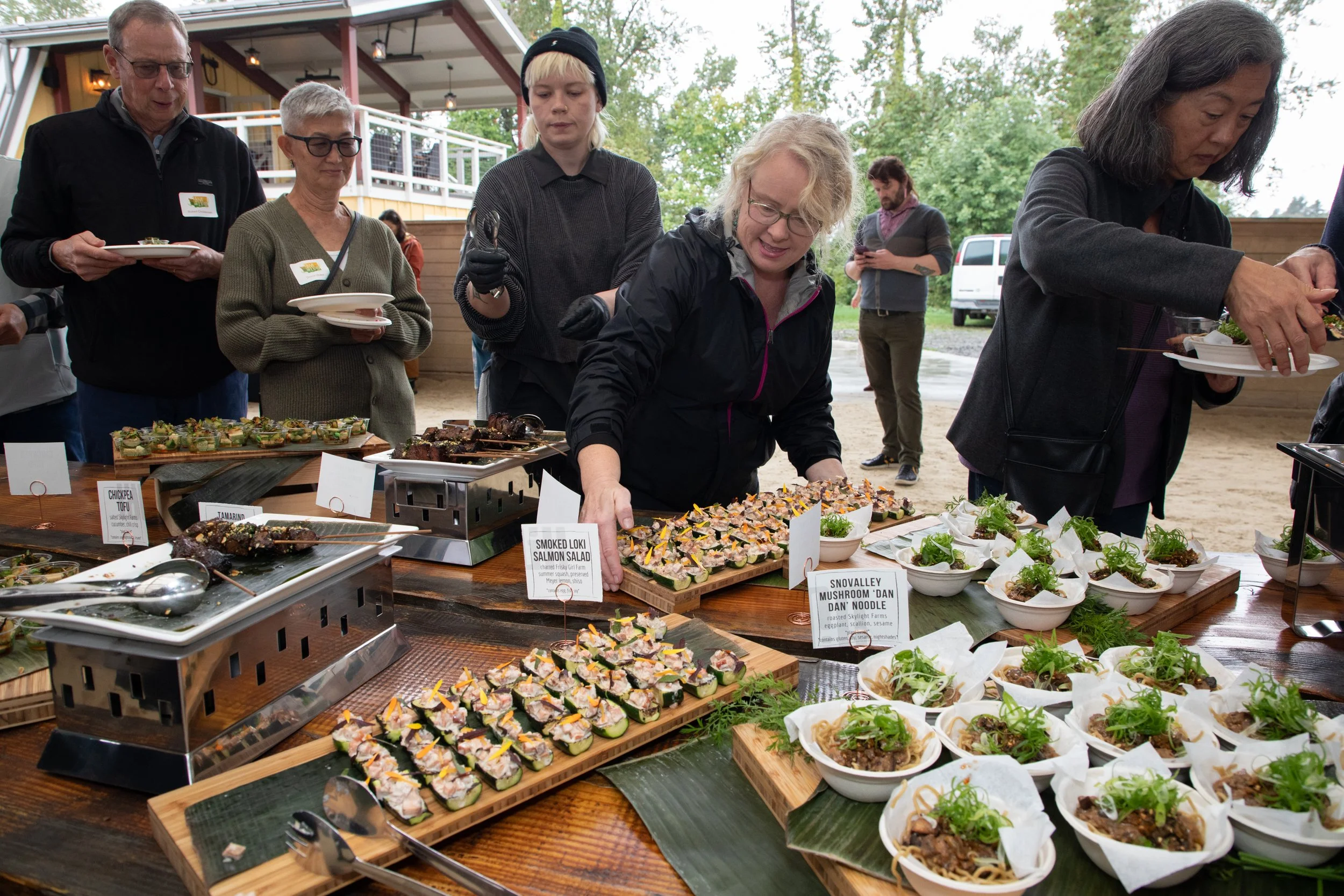 An array of different bites are displayed at a buffet while guests are lining up to grab their selections.