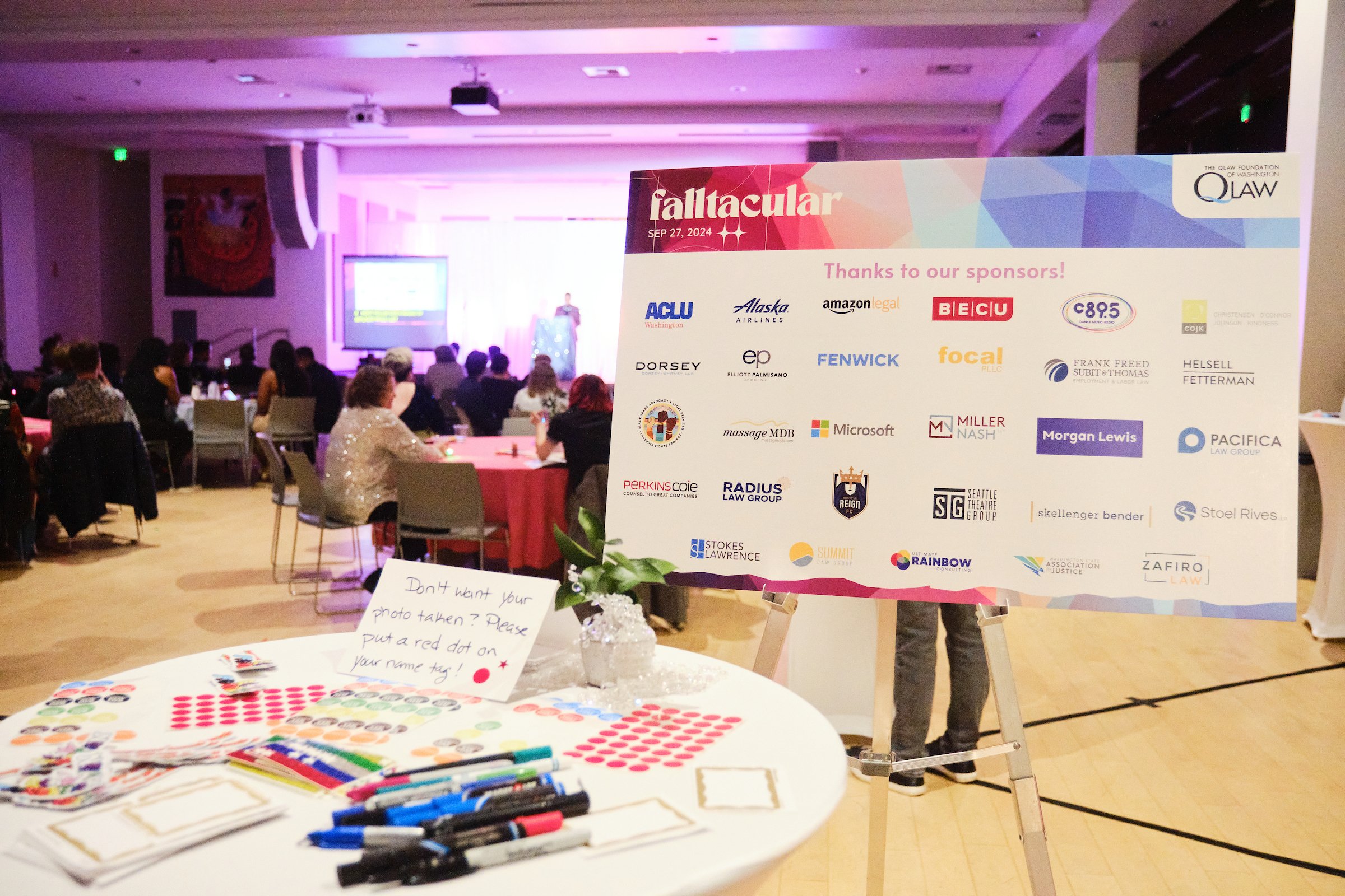 In the foreground we see a bistro table with different colored dot stickers and markers, in the background there is a big signage on a metal easel displaying the different sponsor logos of the event.