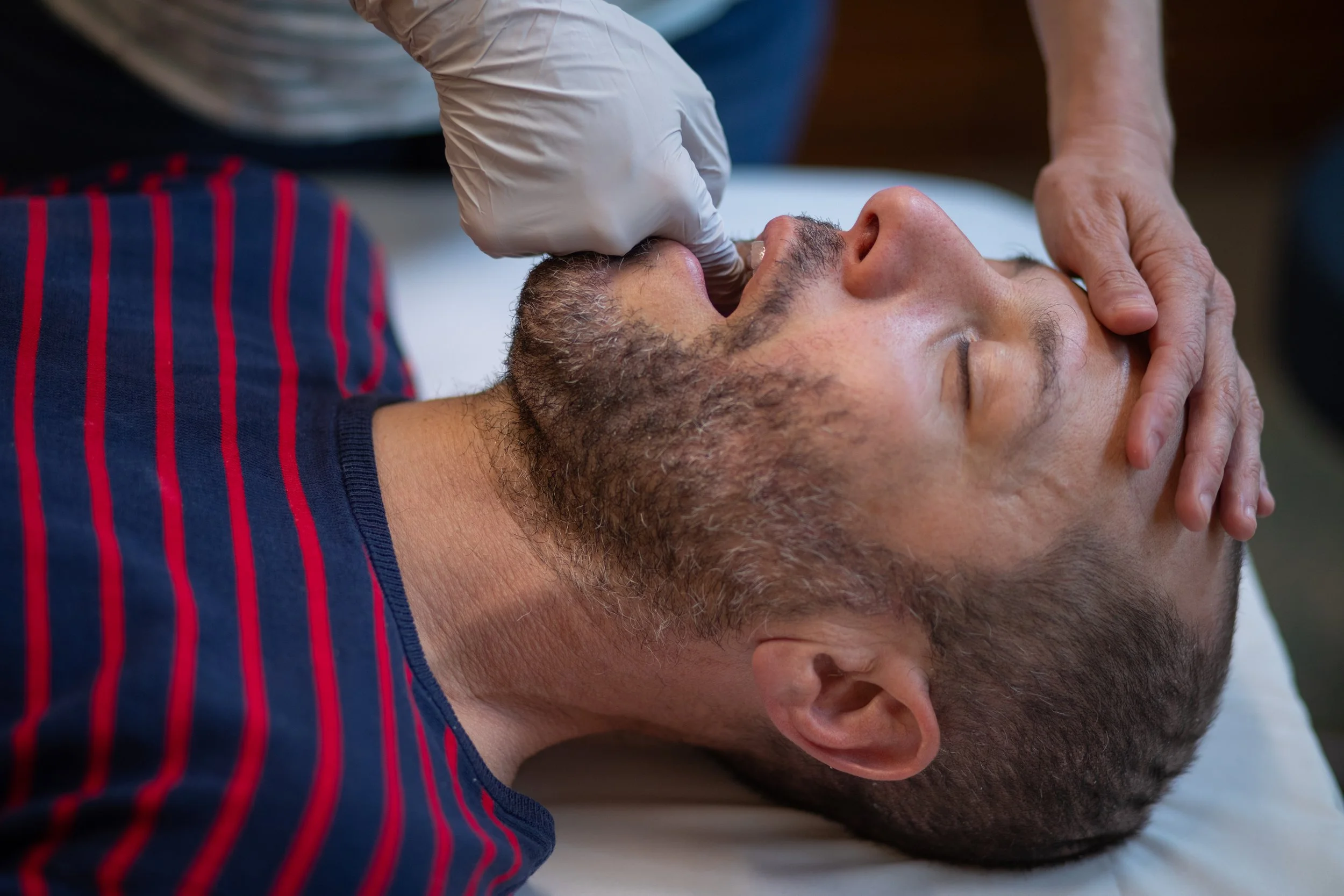Gloved intraoral massage technique for TMJ and jaw tension during a craniosacral session at Halcyon in Seattle SoDo.