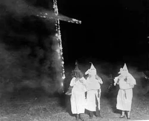 Klan members next to a burning cross