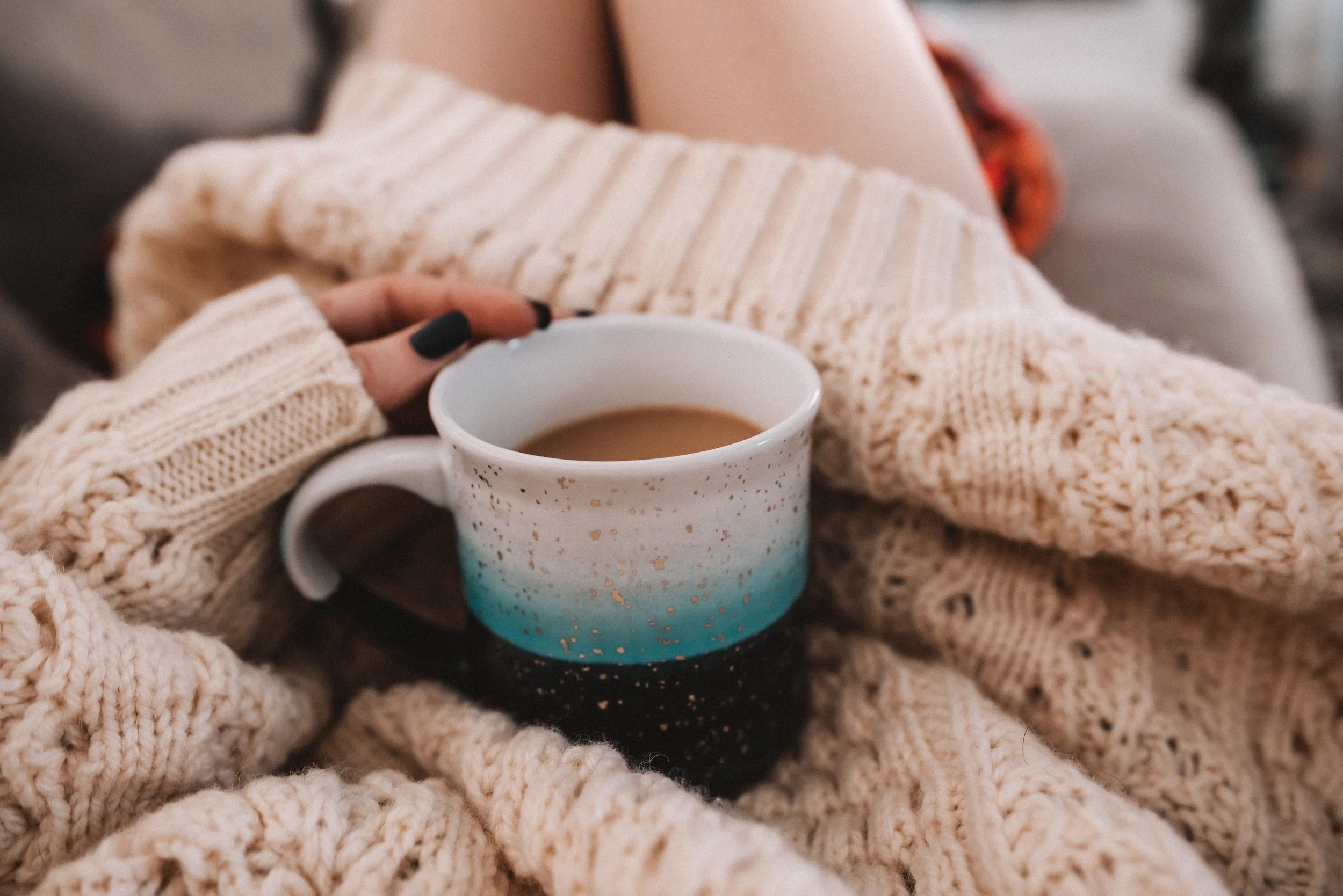 woman sitting in a chunky sweater holding a mug of hot coffee