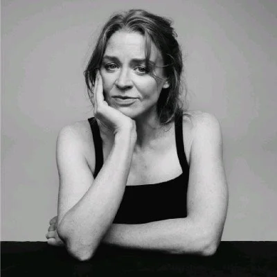 Black and white photo of a woman with shoulder-length hair, resting her head on her hand, looking at the camera with a serious expression.