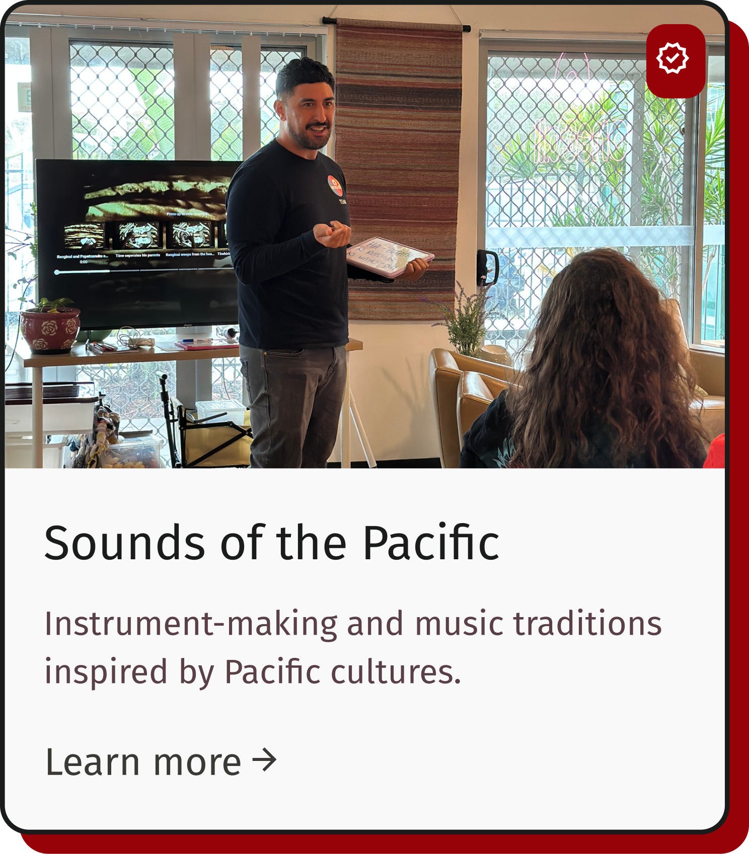 A man demonstrating about Pacific-inspired musical instruments in a meeting room with a large window and a screen behind him.