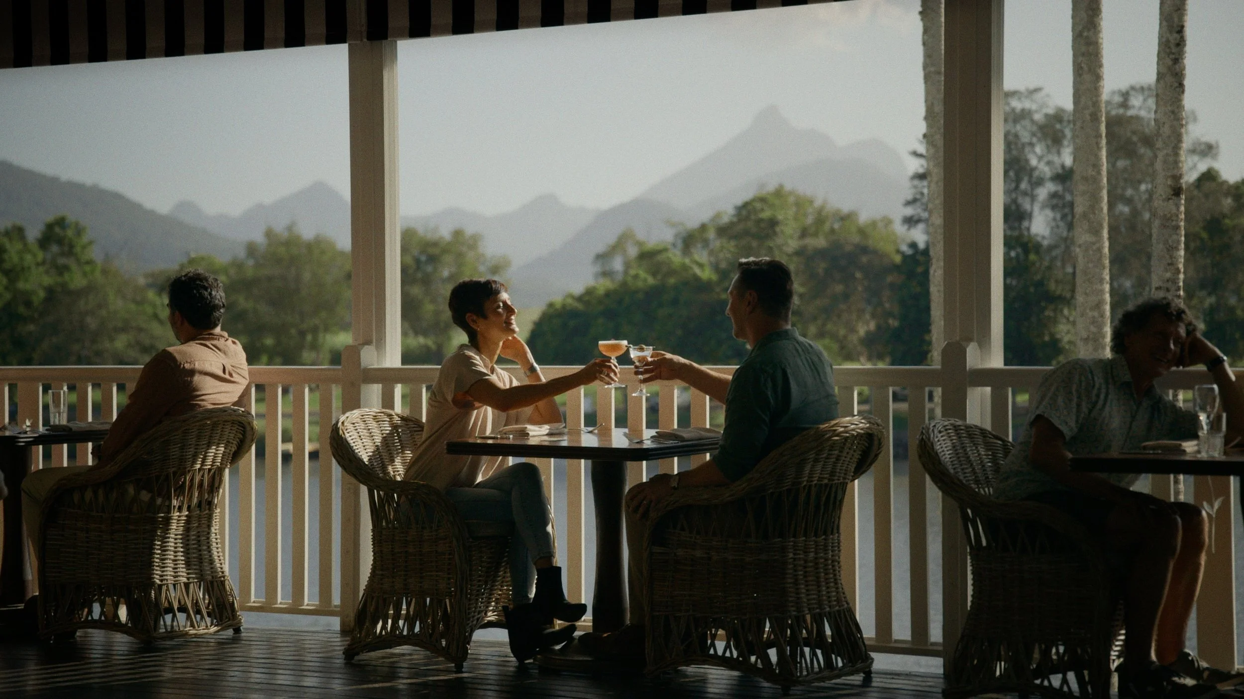 couple on balcony toasting each other with drinks against a mountain range backdrop