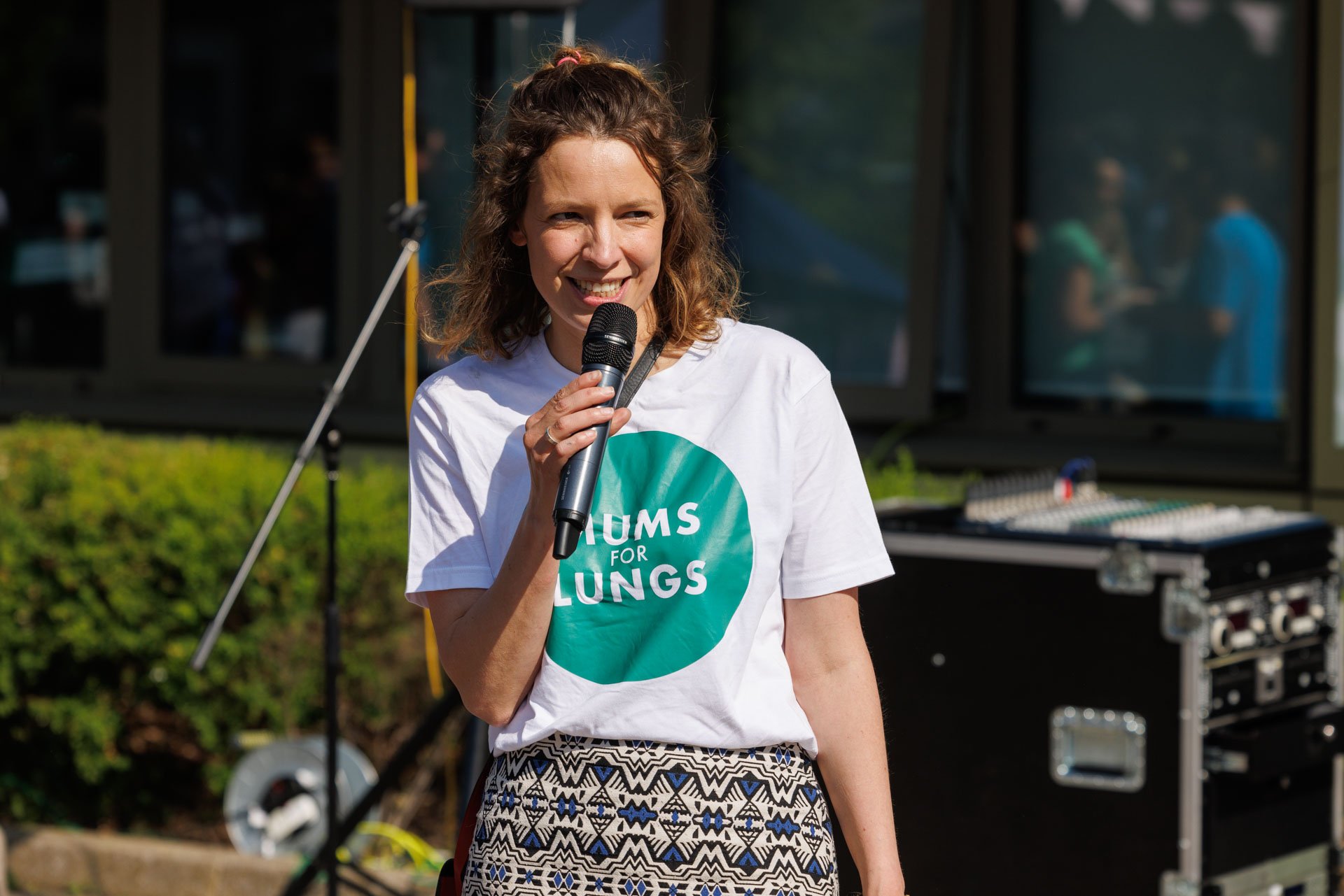 A white woman holding a microphone, smiling and speaking.