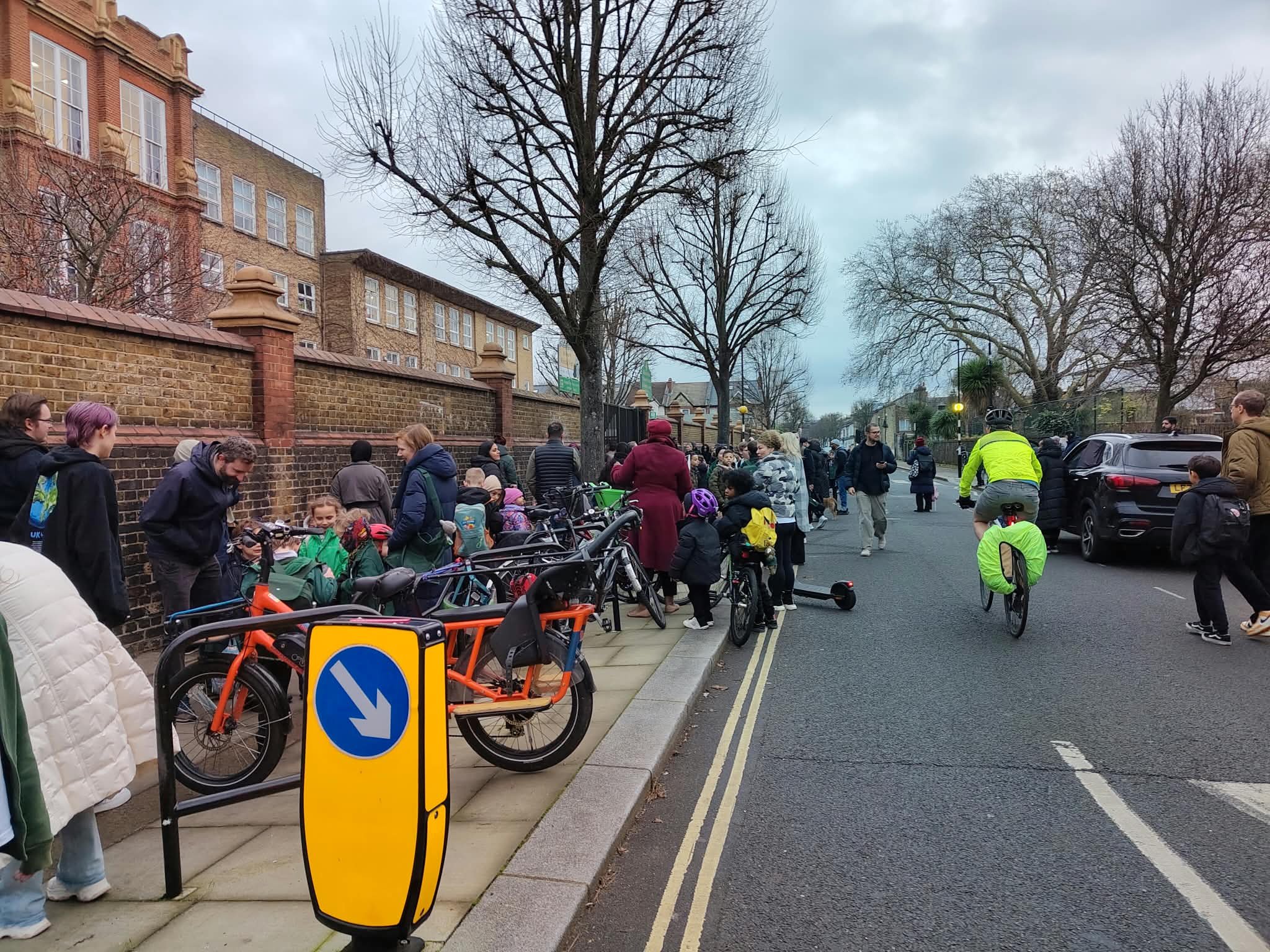 A road outside a school with people on bikes and walking to school.