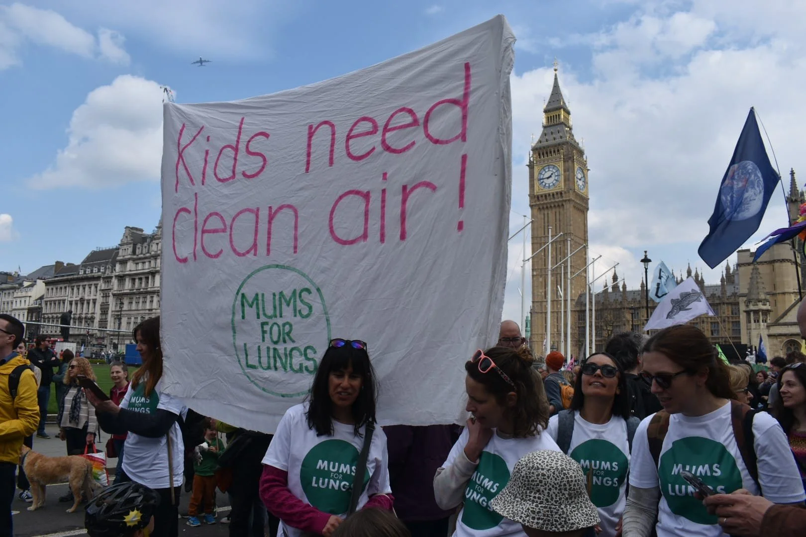 A group of women stand in front of a large white banner that says "Kids need clean air". Big Ben is in the background.
