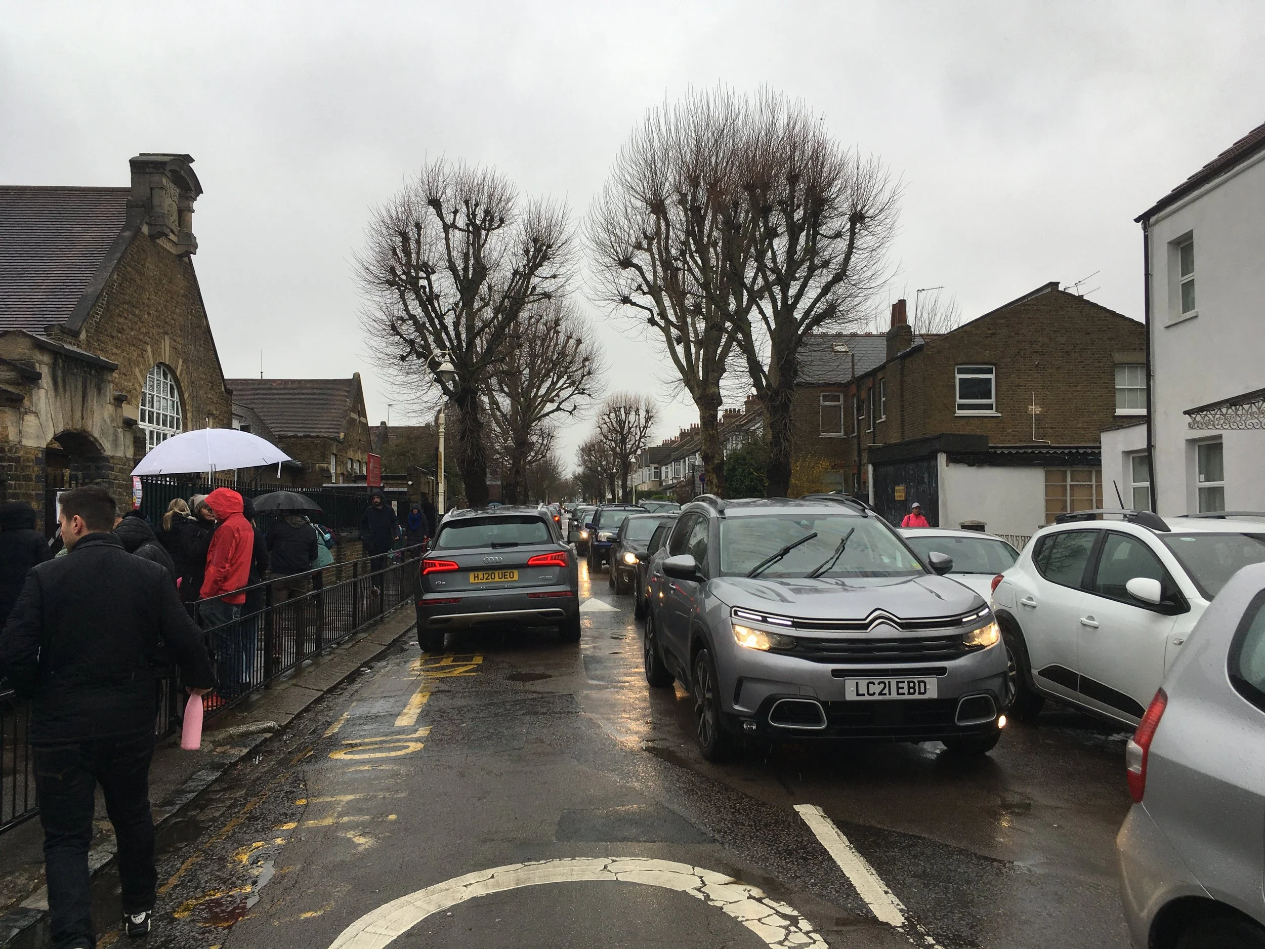A very busy road outside a school, packed with cars.
