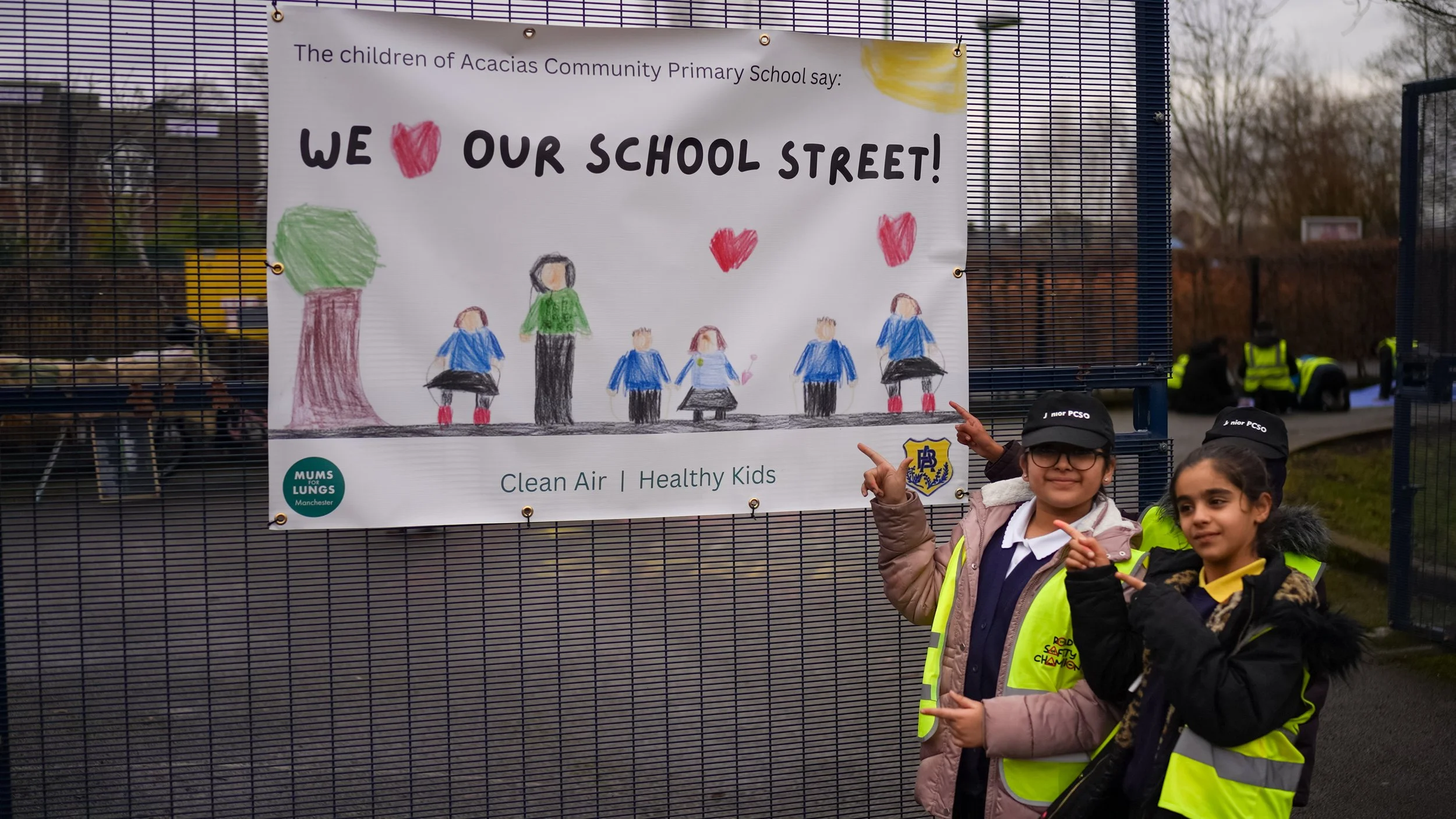 A poster on a school railing, with children pointing at it.