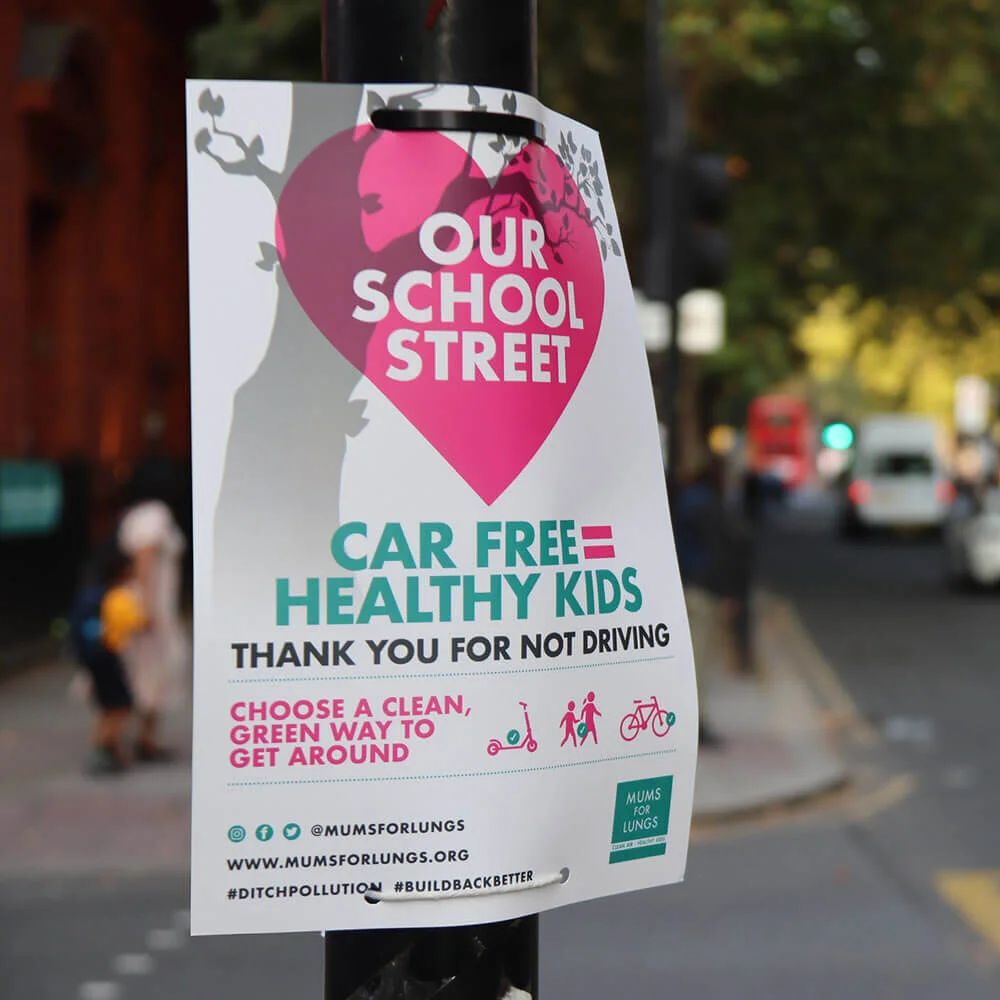 A poster celebrating School Streets is attached to a lamppost. Cars on a busy road can be seen in the background.