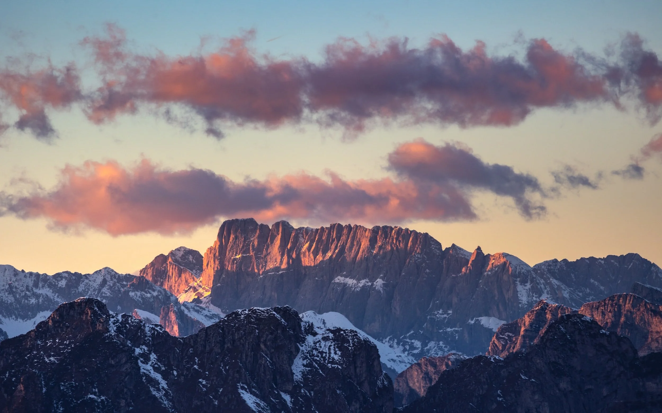 Snow-capped mountain range during sunset with pink clouds in the sky.