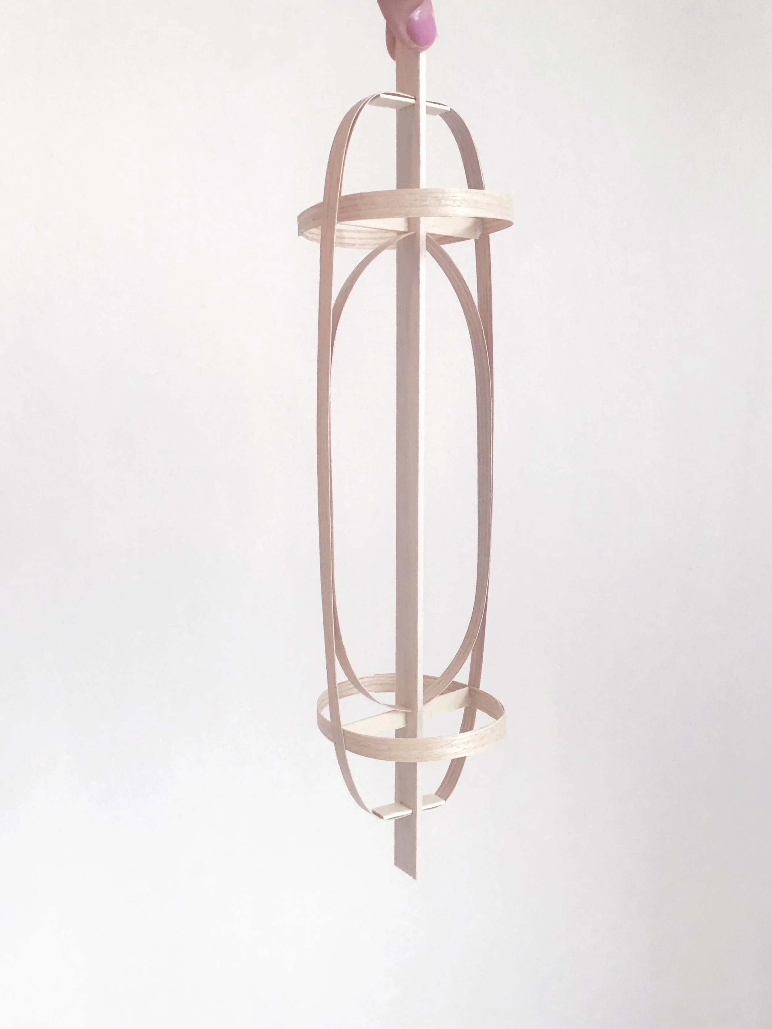 A wooden hanging structure with cylindrical shapes and curved supports, suspended from a person’s finger.