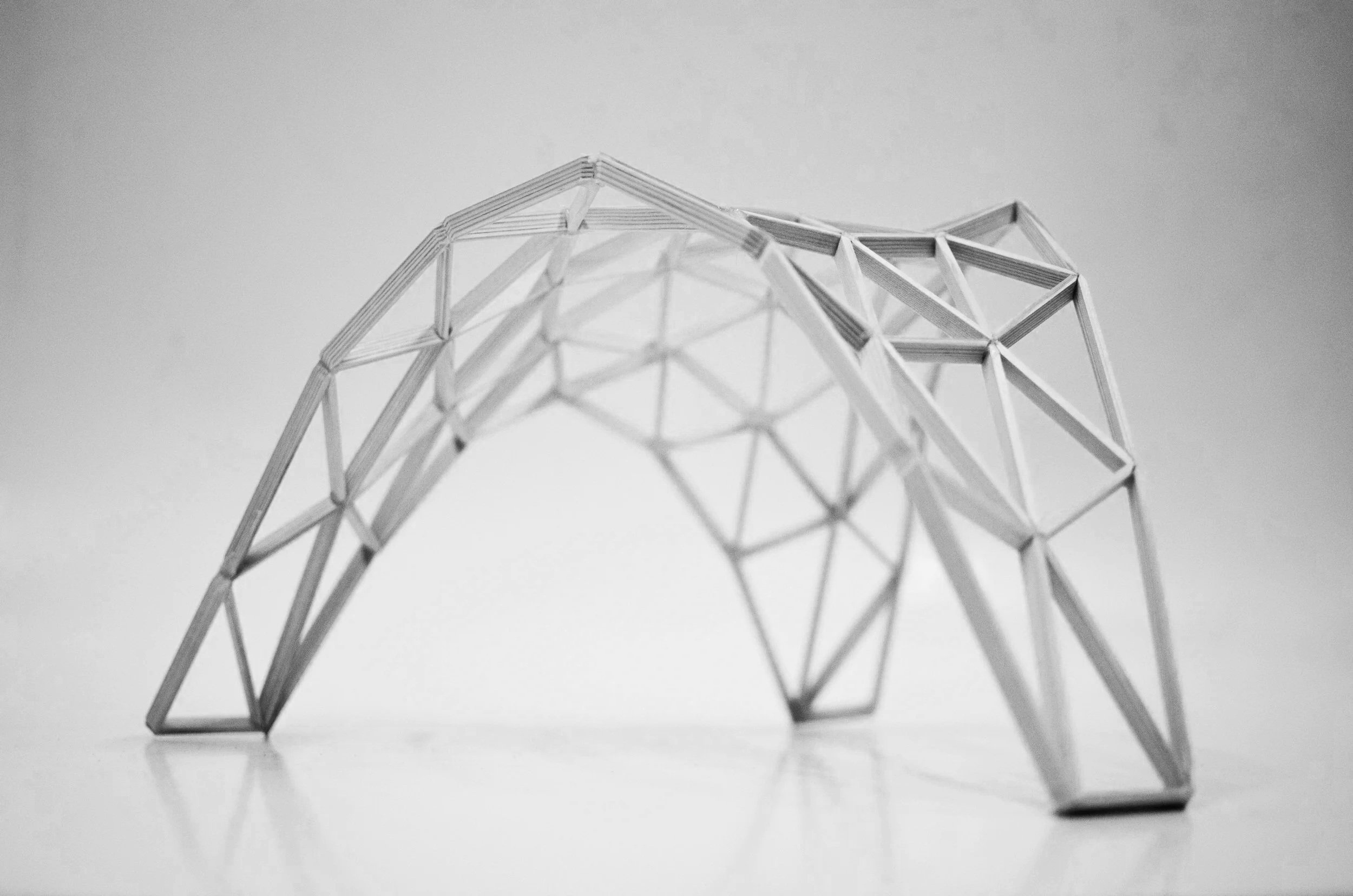 A geometric sculpture of a bear made from interlocking paper or metal strips, arranged in a 3D framework, viewed from below against a plain background.