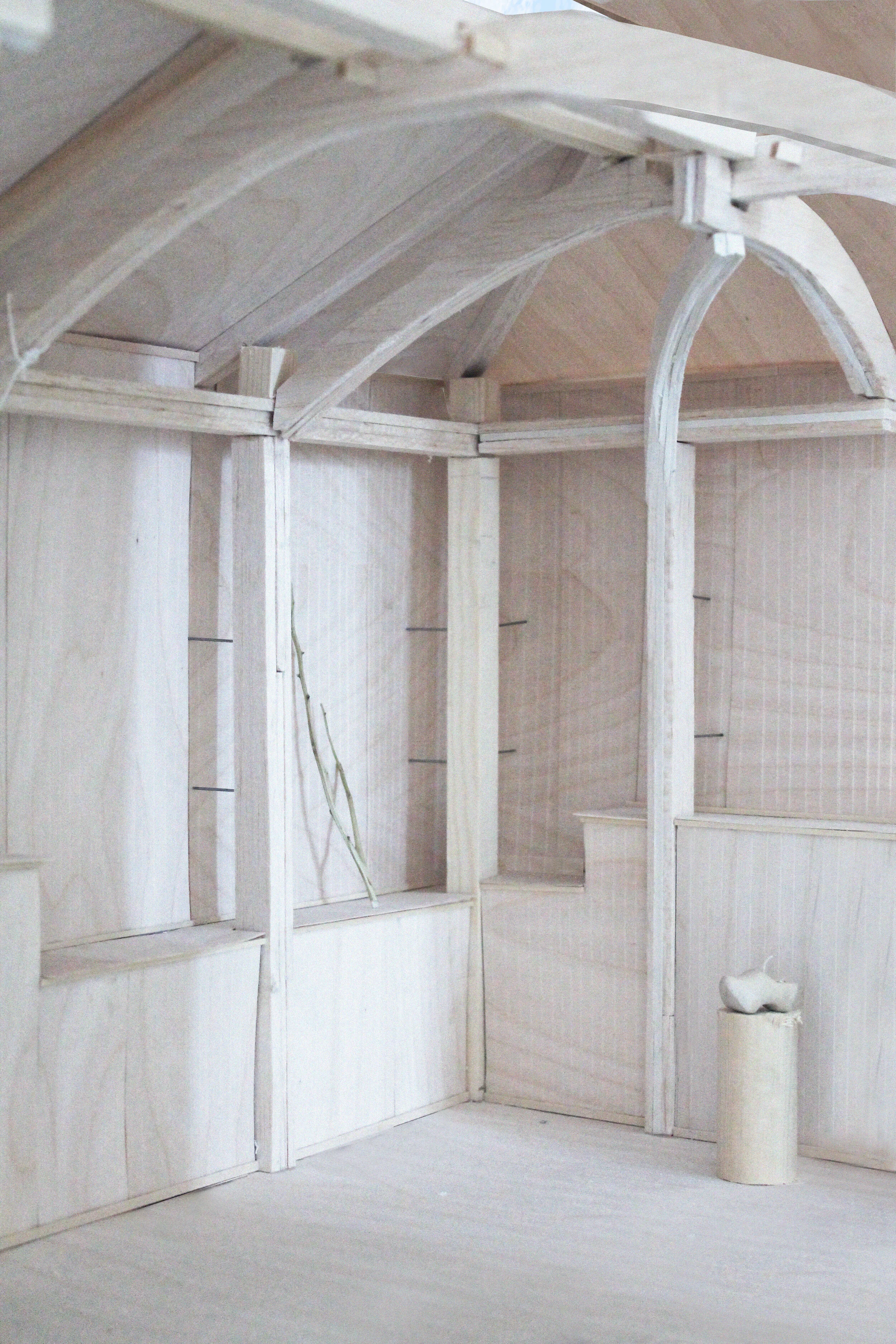 Interior of a wooden structure under construction with unfinished walls and ceiling, and a cylindrical object on a stand.