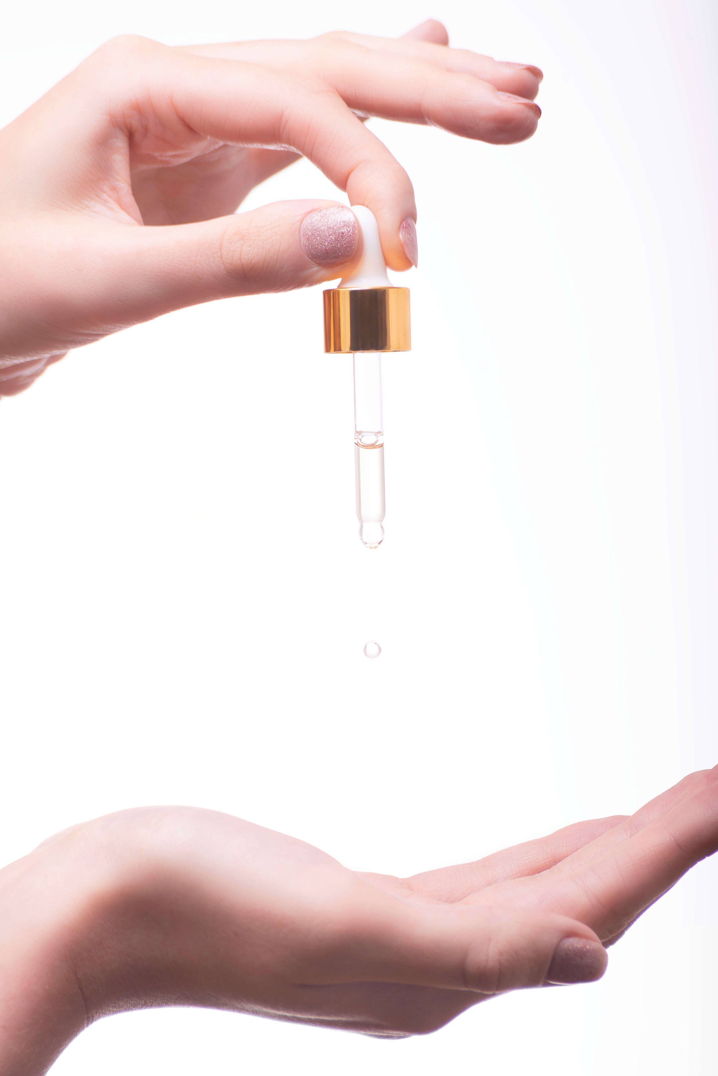 Close-up of hands with a dropper, dispensing liquid onto an open palm.