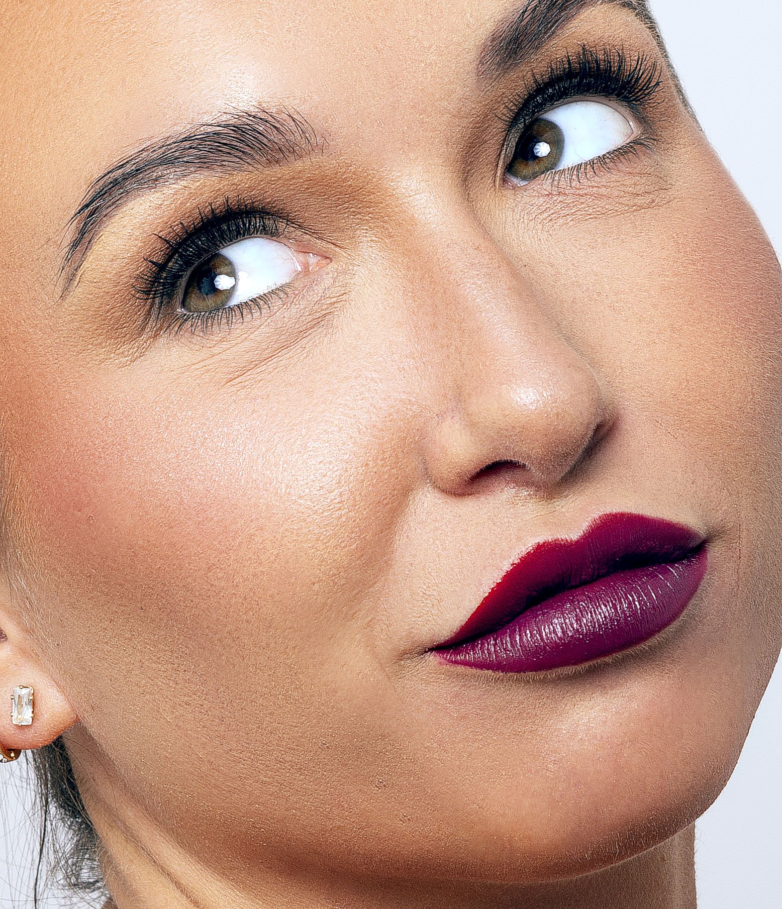Close-up of a woman's face with bold purple lipstick and arched eyebrows, looking upwards.
