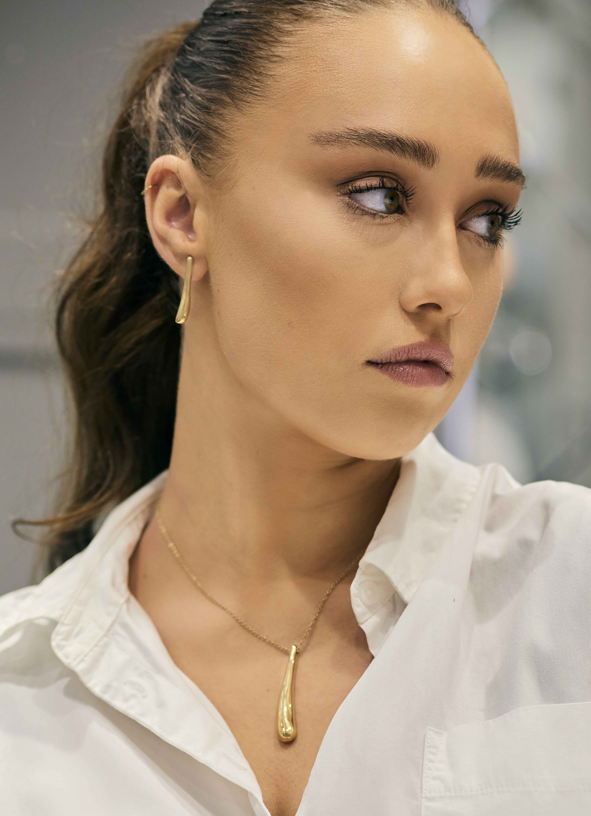 Woman with gold earring and pendant wearing a white shirt