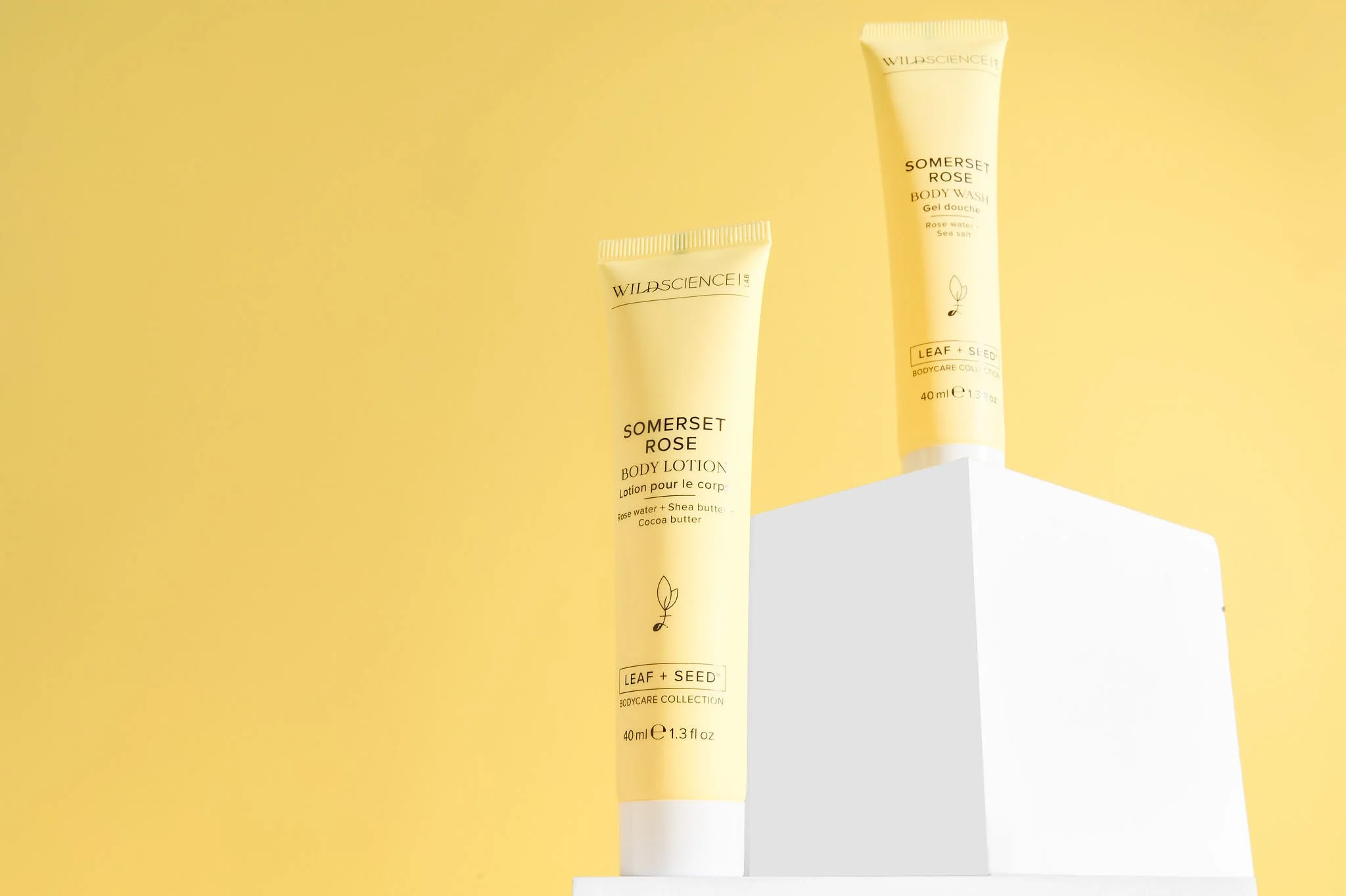 Two tubes of Somerset Rose body care products from Wild Science on a white pedestal against a yellow background, one body lotion and one body wash.