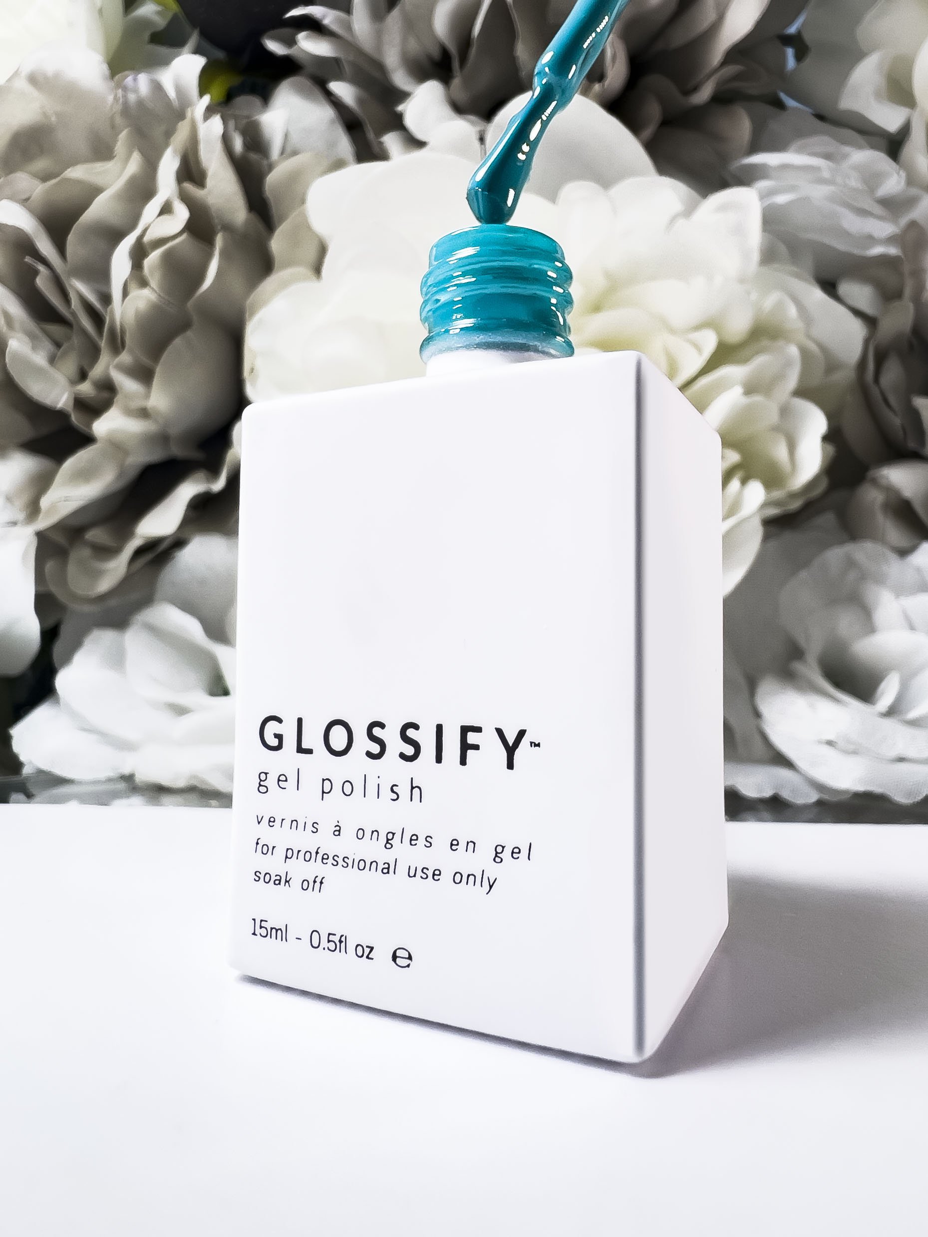 Glossify gel nail polish bottle with turquoise polish brush, floral background.
