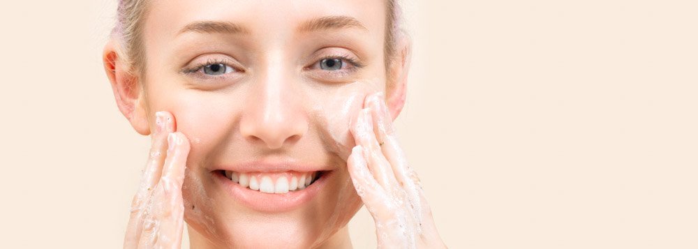 Person applying facial cleanser on face, smiling.