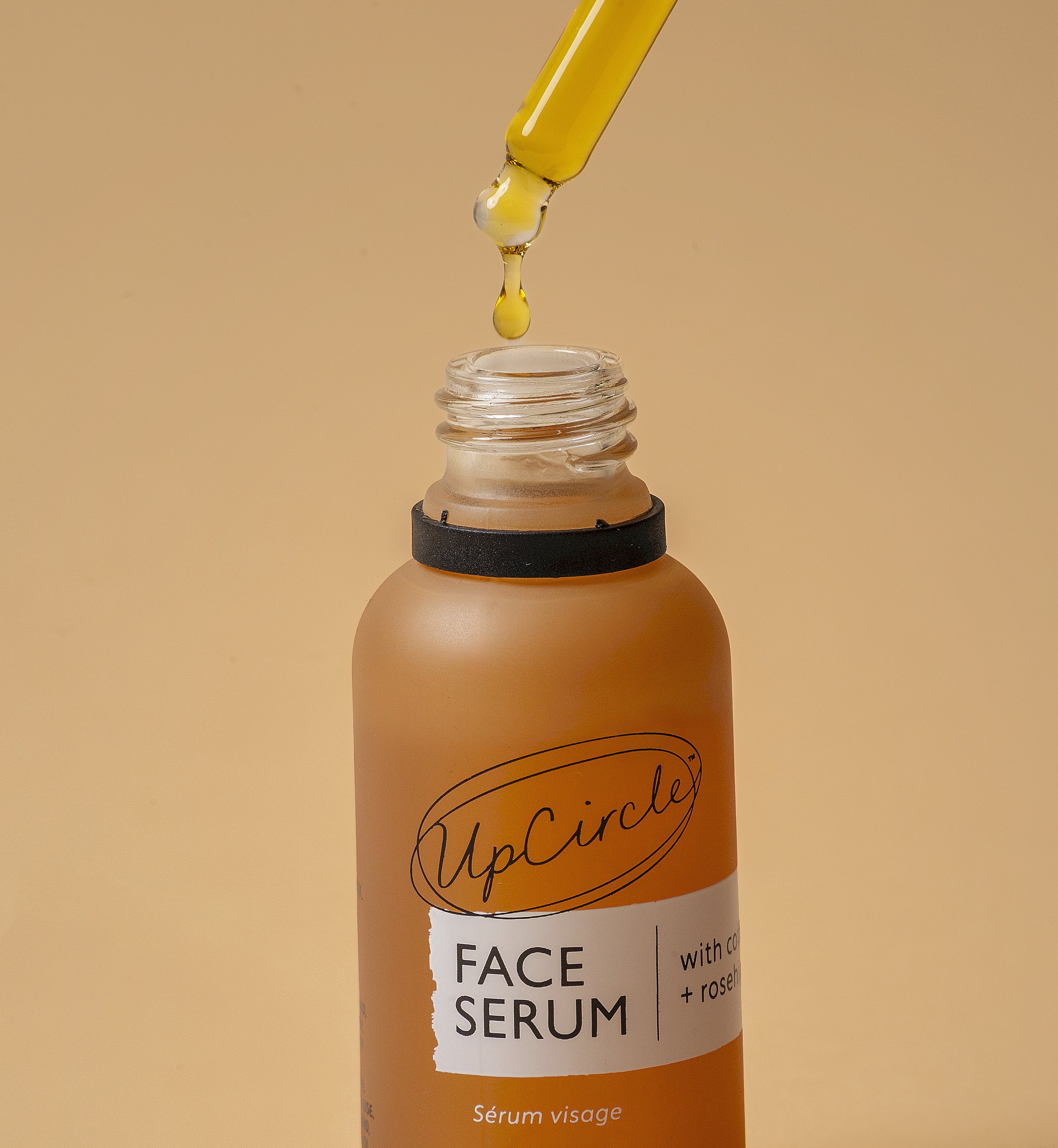 Bottle of UpCircle face serum with a dropper dispensing liquid against a beige background.