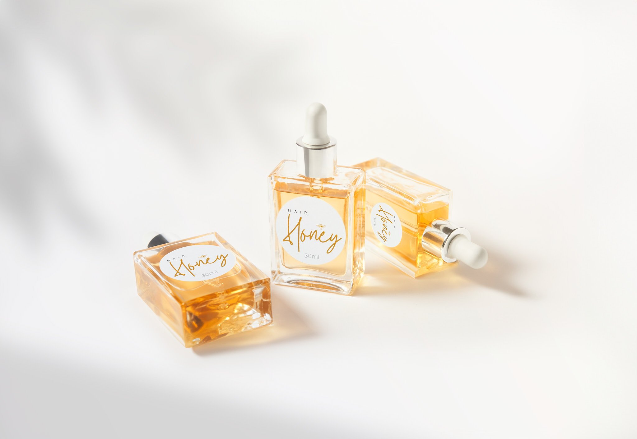 Three bottles of hair oil labeled "Hair Honey" with droppers, containing amber-colored liquid.
