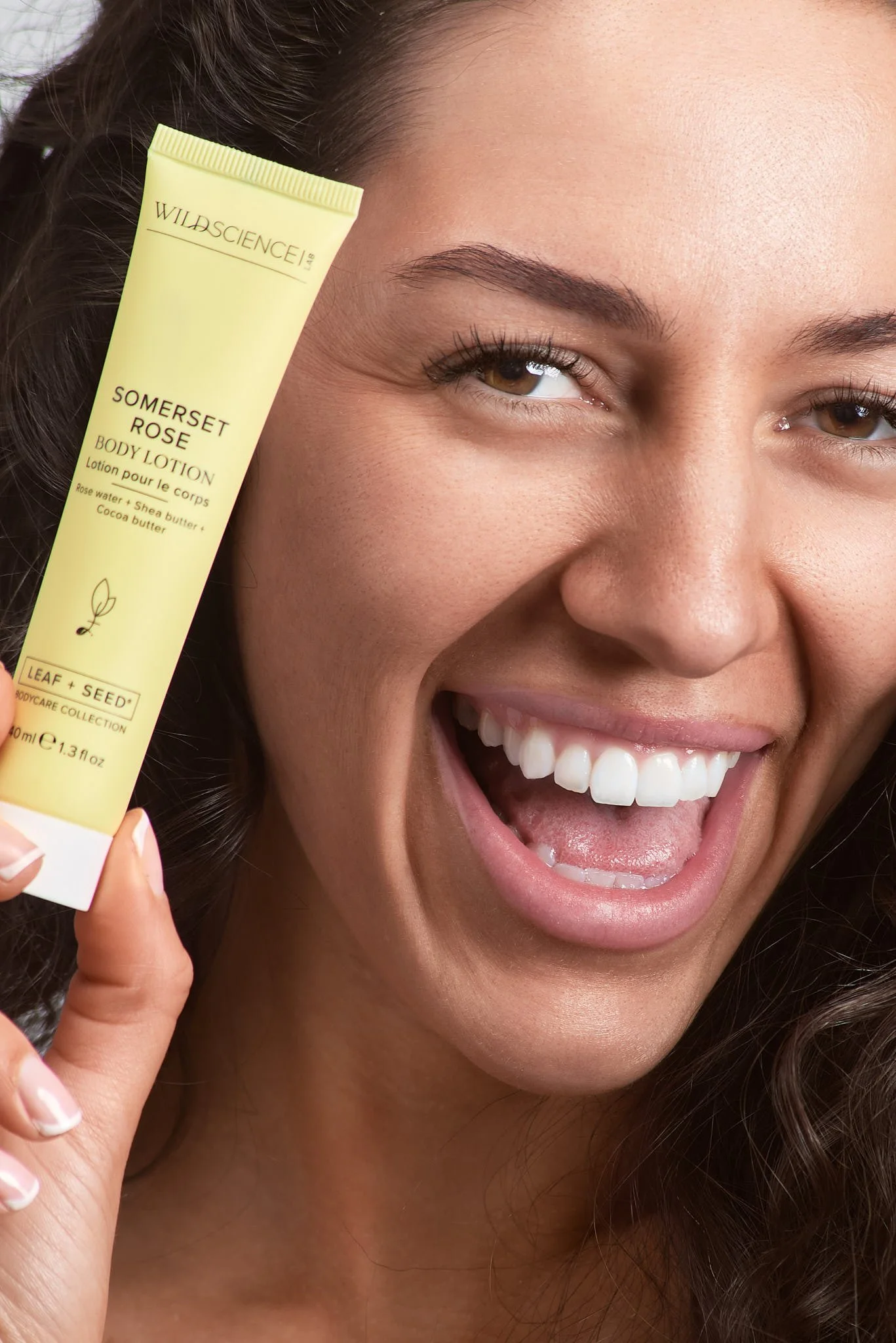 A woman smiling while holding a tube of Somerset Rose body lotion close to her face.