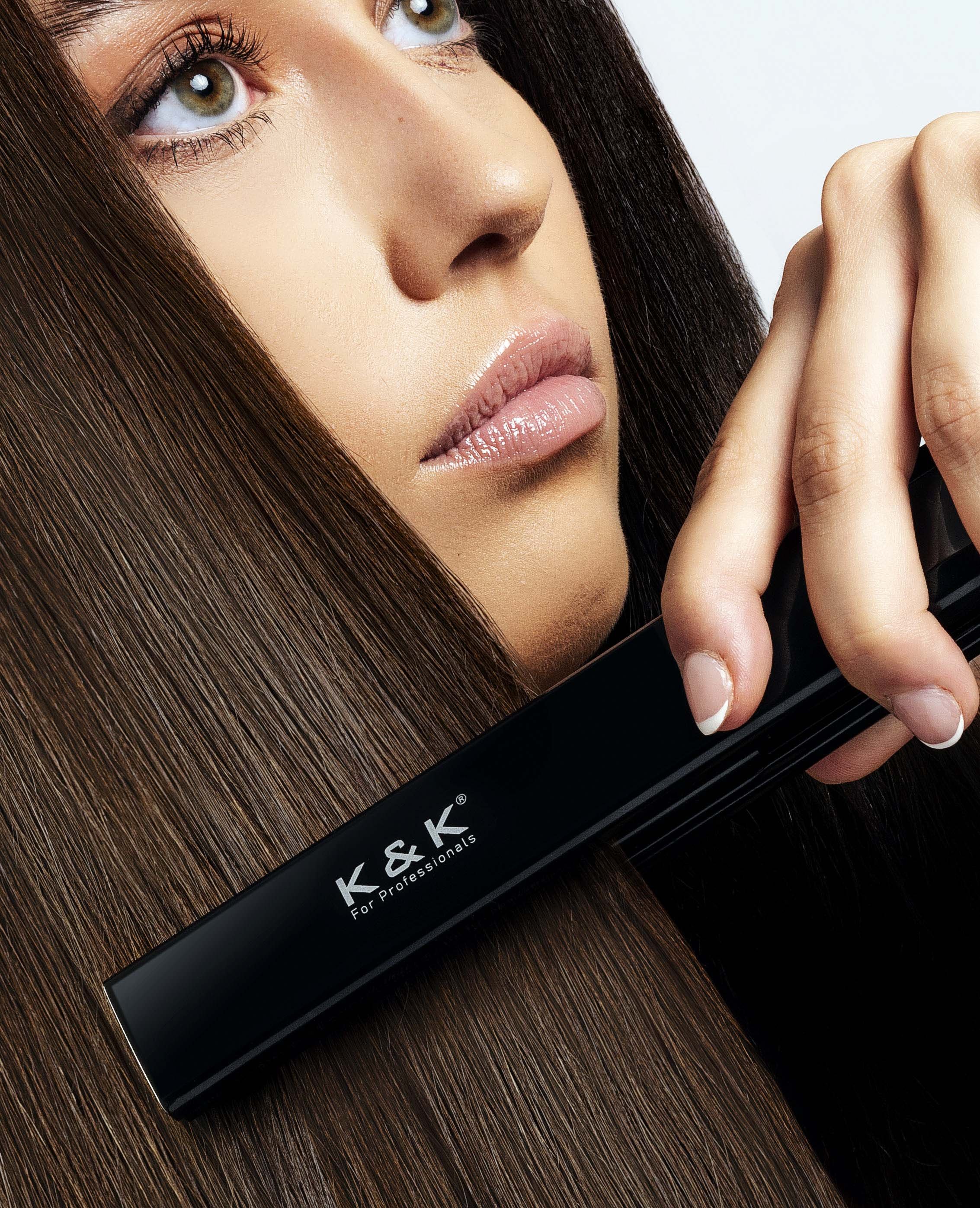 Close-up of a woman using a K&K hair straightener on long, smooth brown hair.