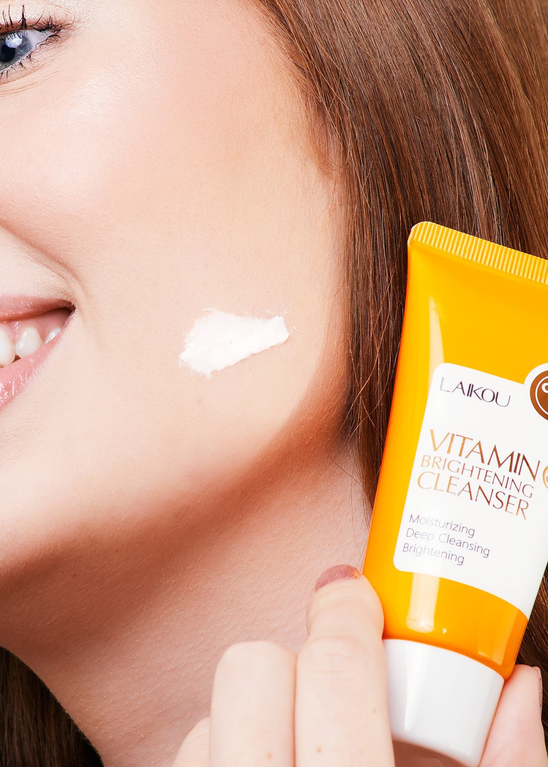 Close-up of a woman applying Vitamin C brightening cleanser to her cheek from an orange tube labeled "Laikou Vitamin C Brightening Cleanser."