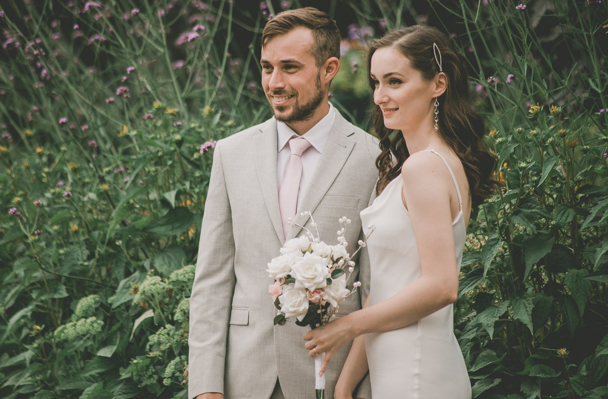 Bride and groom posing outdoors with flowers in the background.