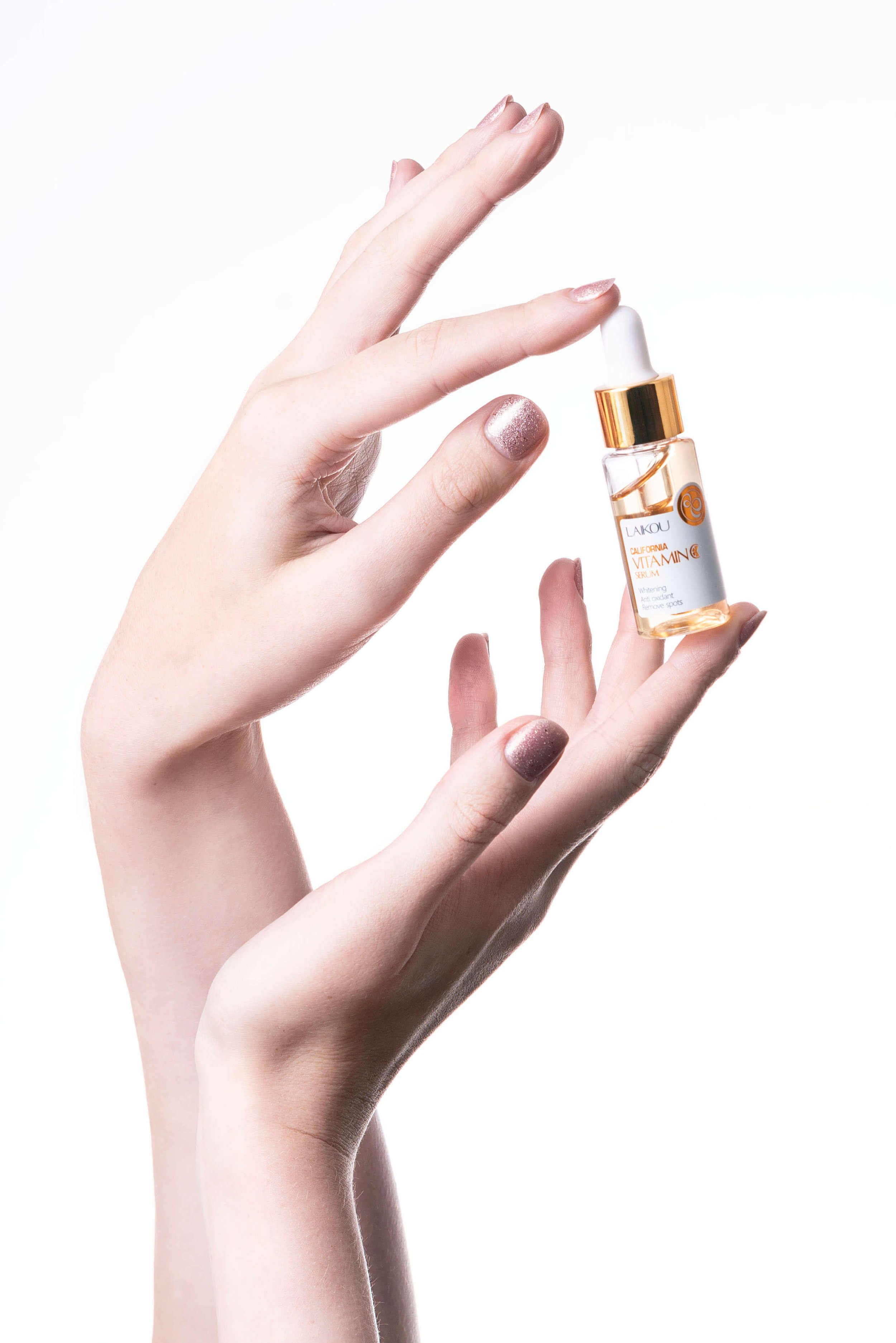 Close-up of two hands holding a small dropper bottle labeled "Vitamin C Serum" against a white background.