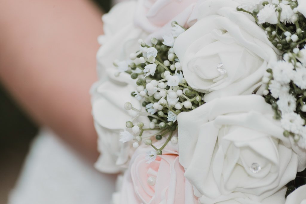 Close-up of an artificial bridal bouquet with white roses and small white flowers.
