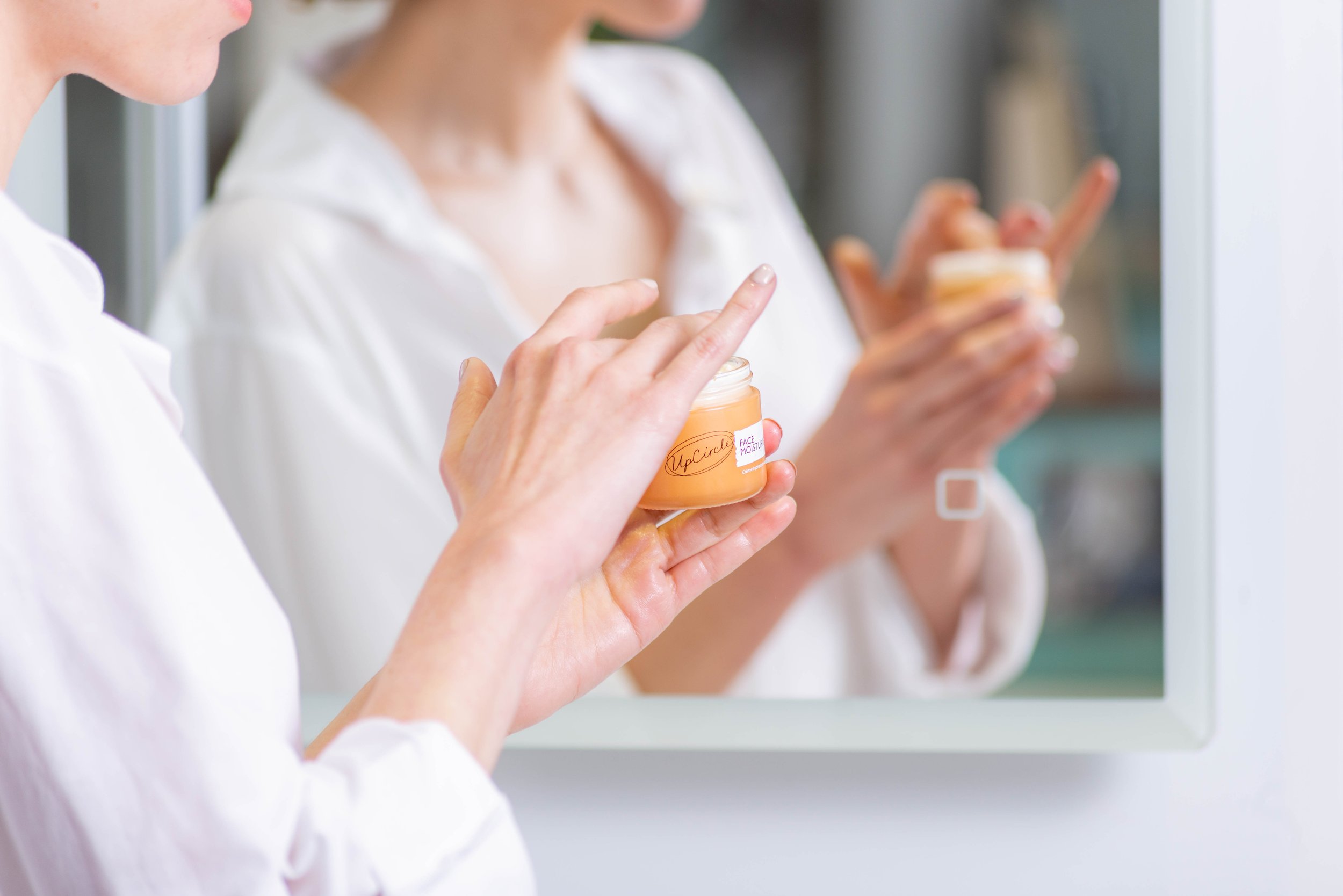 Person applying face moisturizer in front of a mirror.