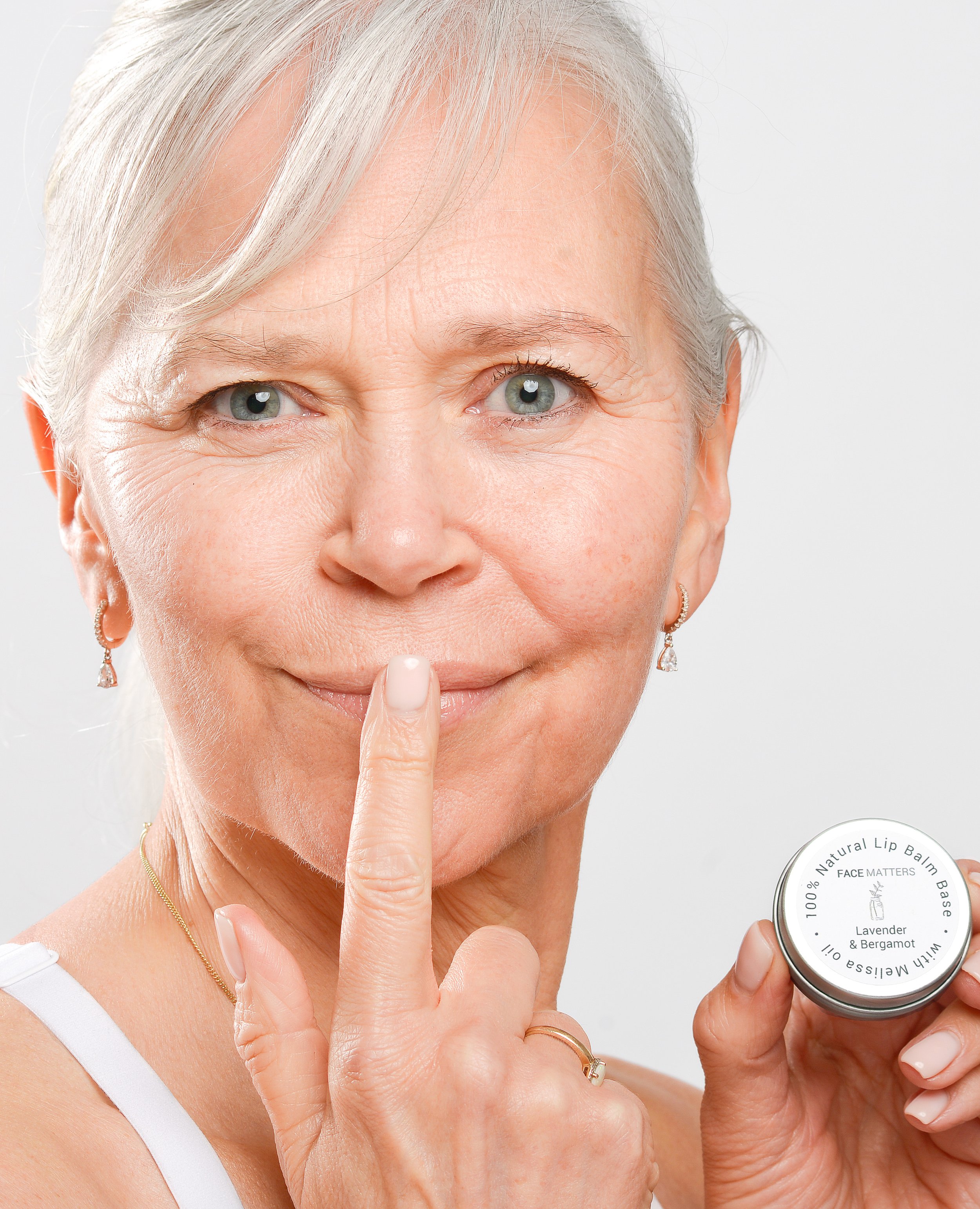 Older woman applying lip balm from a small container, displaying product.