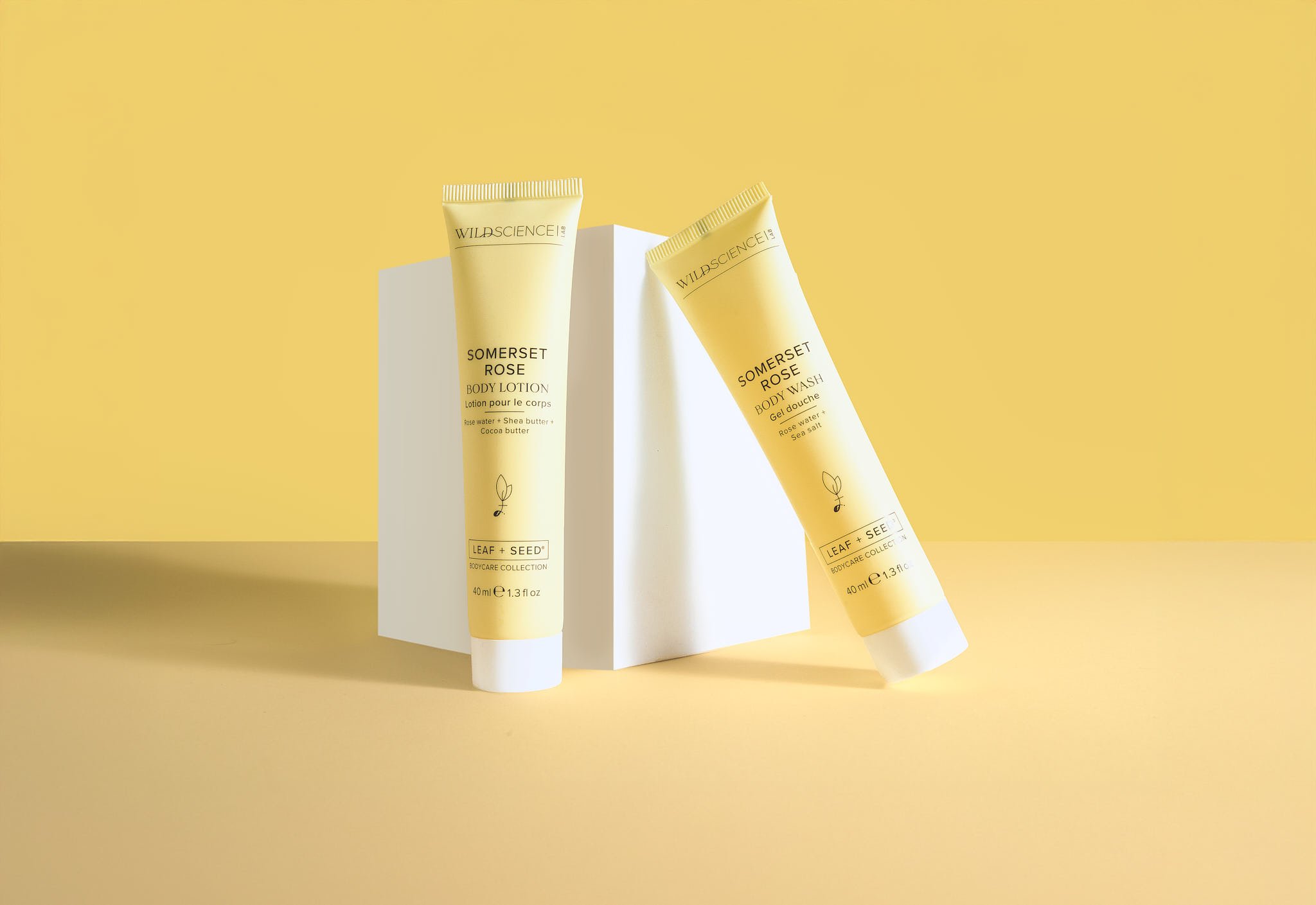 Two tubes of Wild Science Somerset Rose skincare products, body lotion and body wash, placed on a white block against a yellow background.