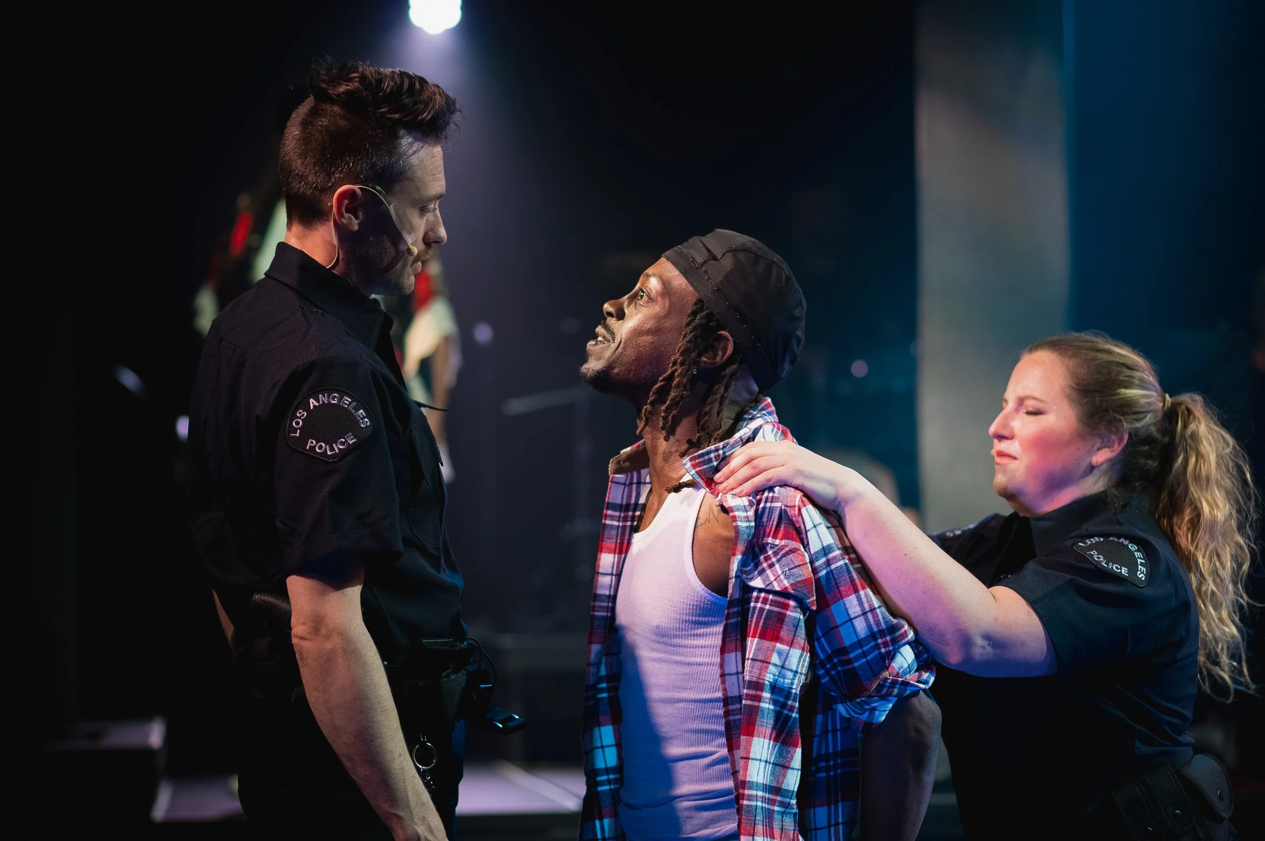 A police officer in Los Angeles talking to a distressed man with dreadlocks and a plaid shirt, while a woman in uniform comforts a woman with blonde hair.