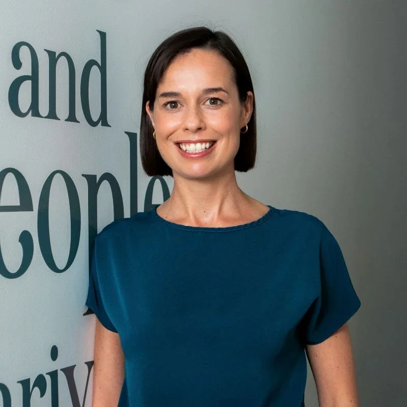 A woman smiling in front of a wall with large text reading 'and people'.
