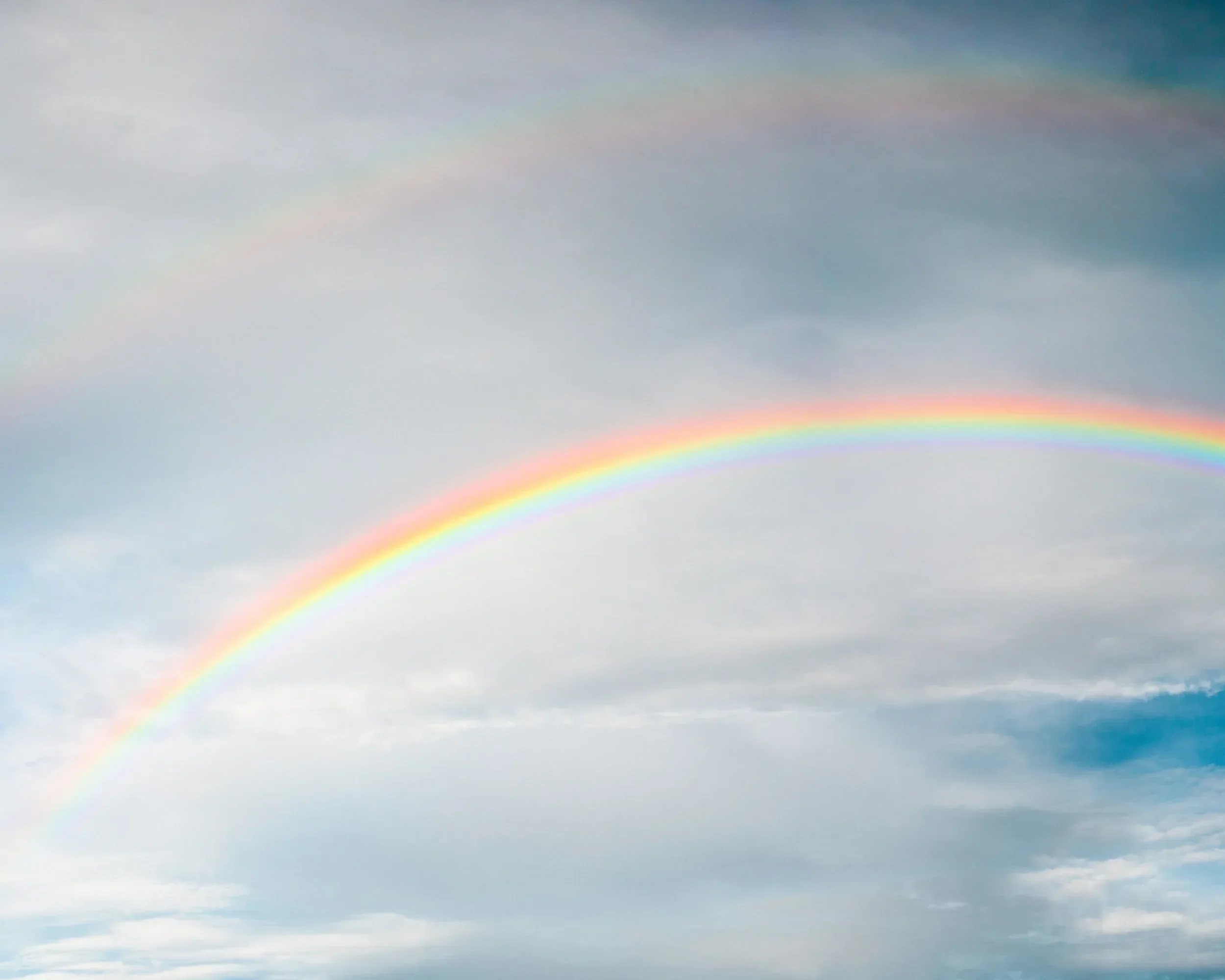 A double rainbow in a cloudy sky with various shades of blue and gray.