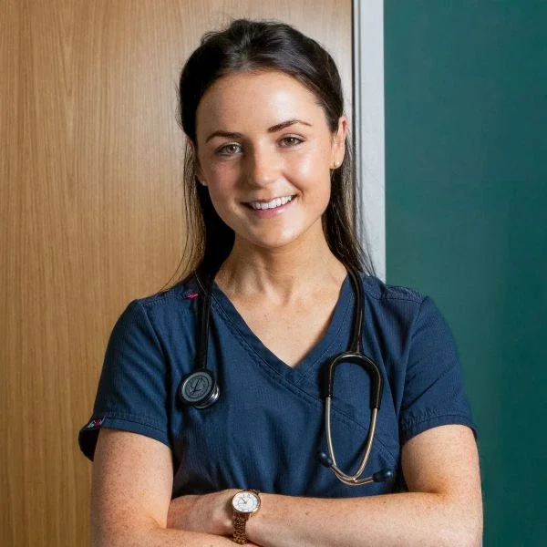 A female healthcare professional wearing navy scrubs and a stethoscope around her neck, smiling with her arms crossed.
