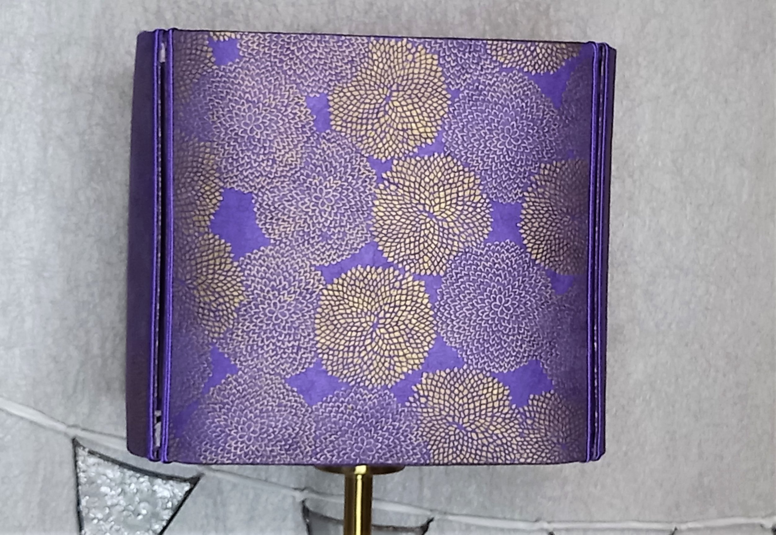 Abat- jour carré coins arrondis papier népalais motif floral doré sur fond violet clair. Travaillé sur 4 faces indépendantes bordées de soutache violette laissant passer la lumière dans les angles. Pourpré en version allumée. 50 €.
A retrouver sur l