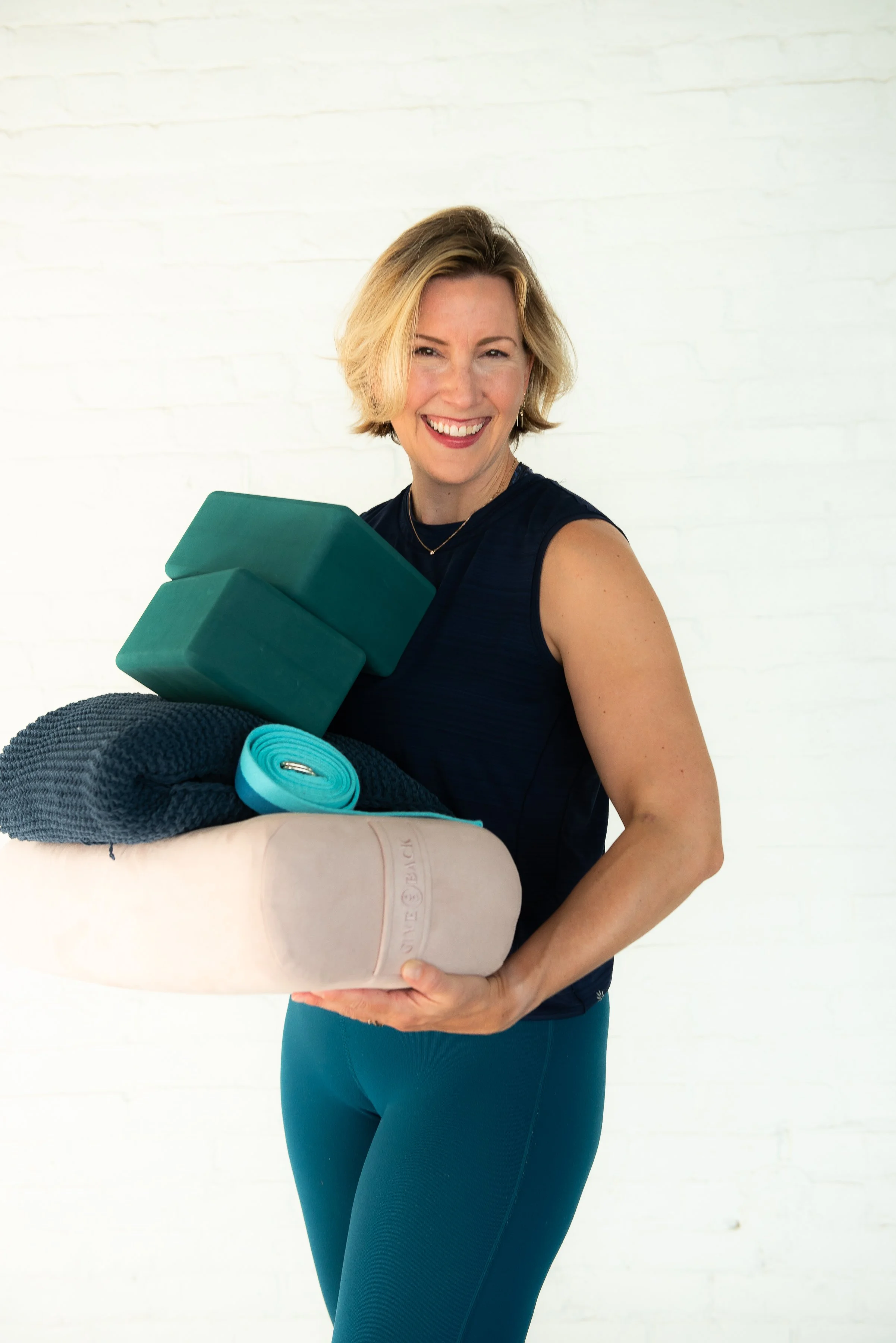 Kelley Curran, yoga instructor in the Hudson Valley, holding yoga props and smiling in a bright studio space