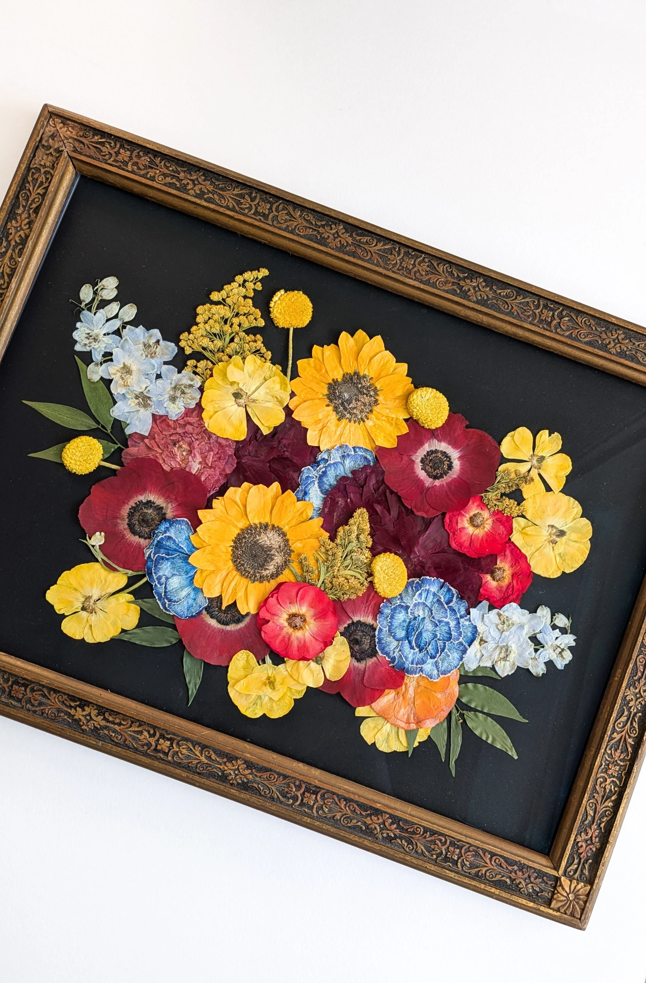 Pressed flower arrangement with sunflowers, poppies, hydrangeas, and other flowers in an antique frame.