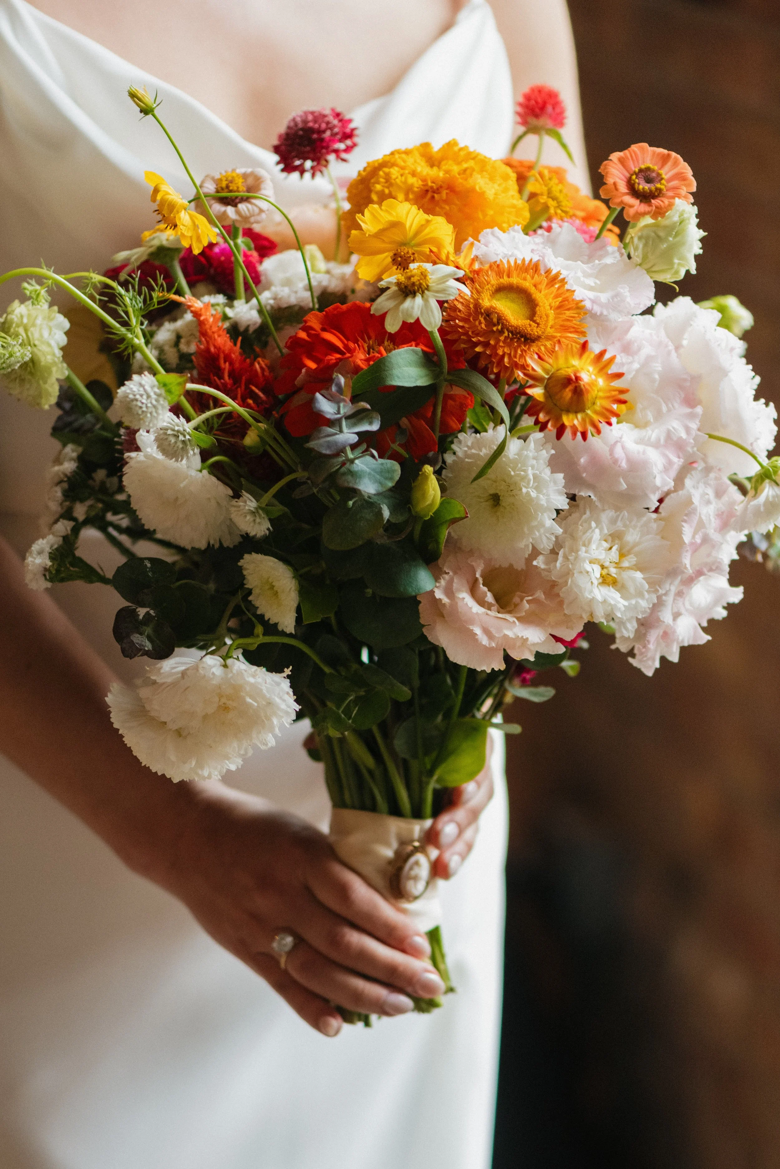 A bride in a white dress holding a large bouquet of colorful flowers, including white, pink, yellow, and orange blooms.