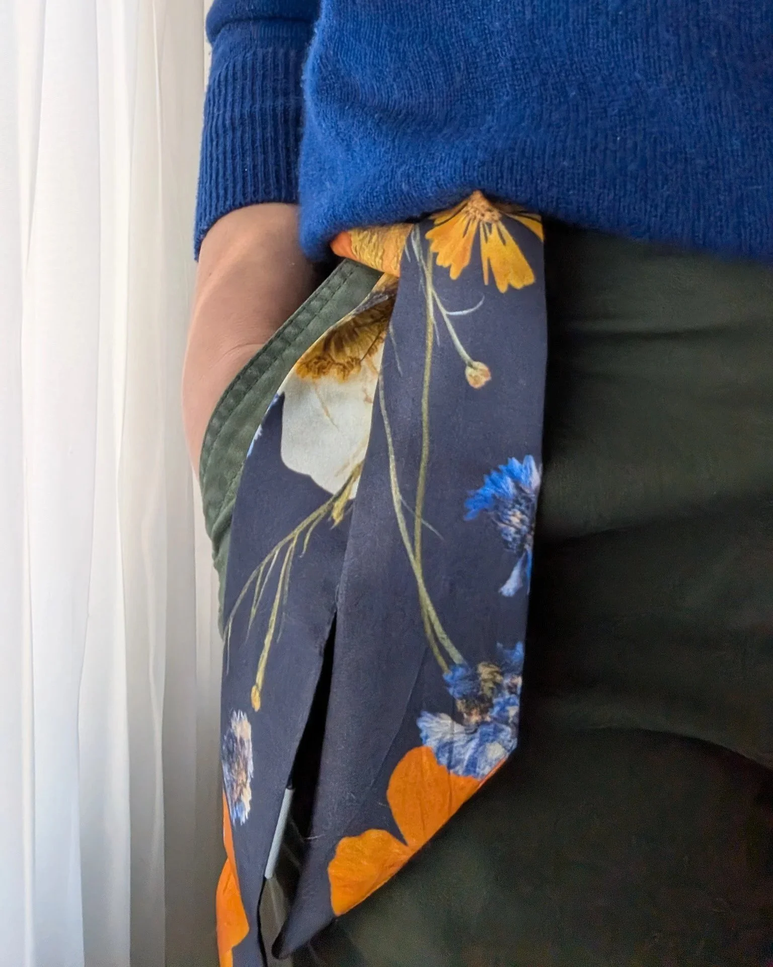 Person wearing a blue sweater and green pants with a floral scarf hanging over the edge.